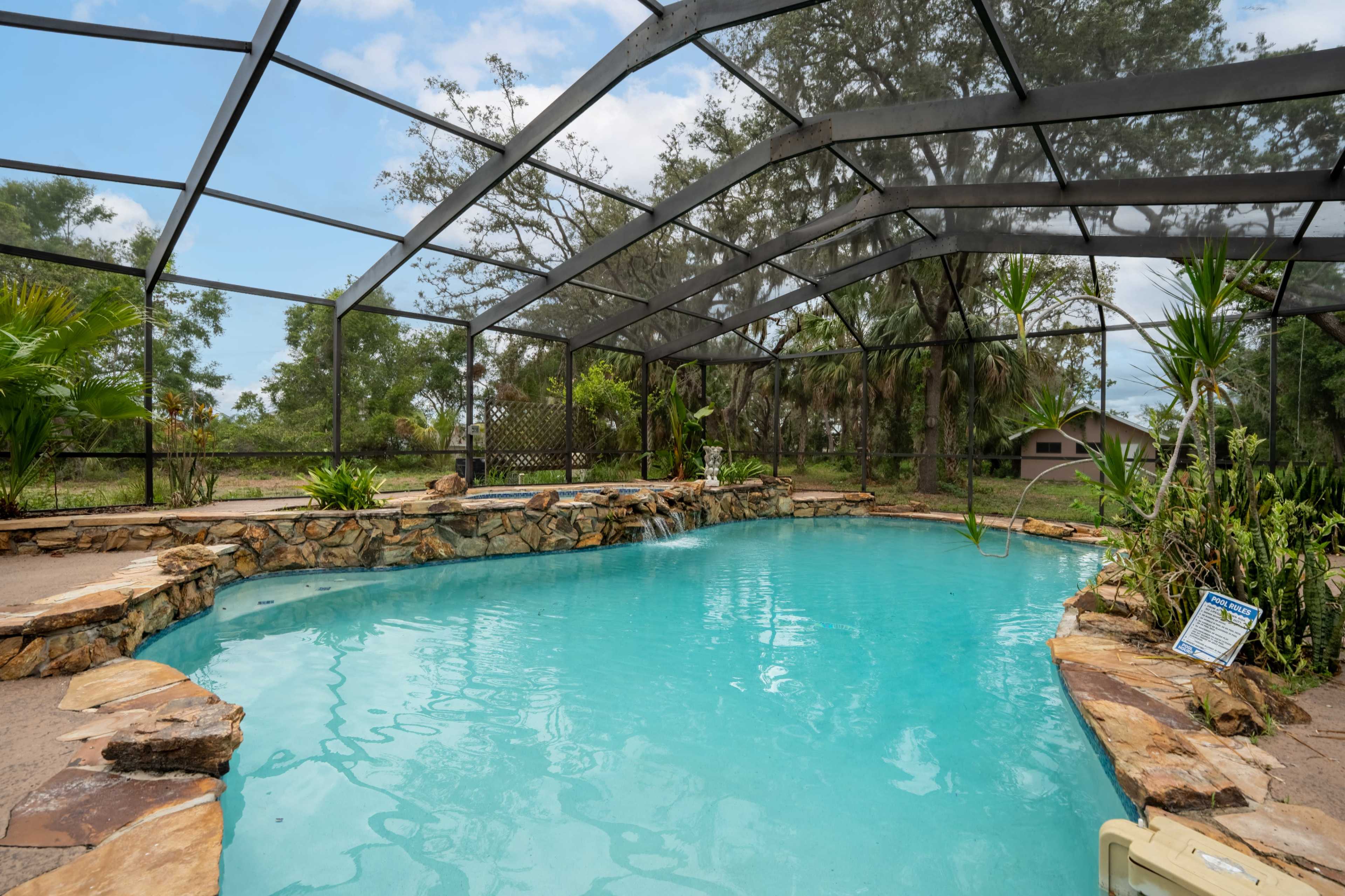 The image shows a screened-in pool area surrounded by rock features and tropical plants.
