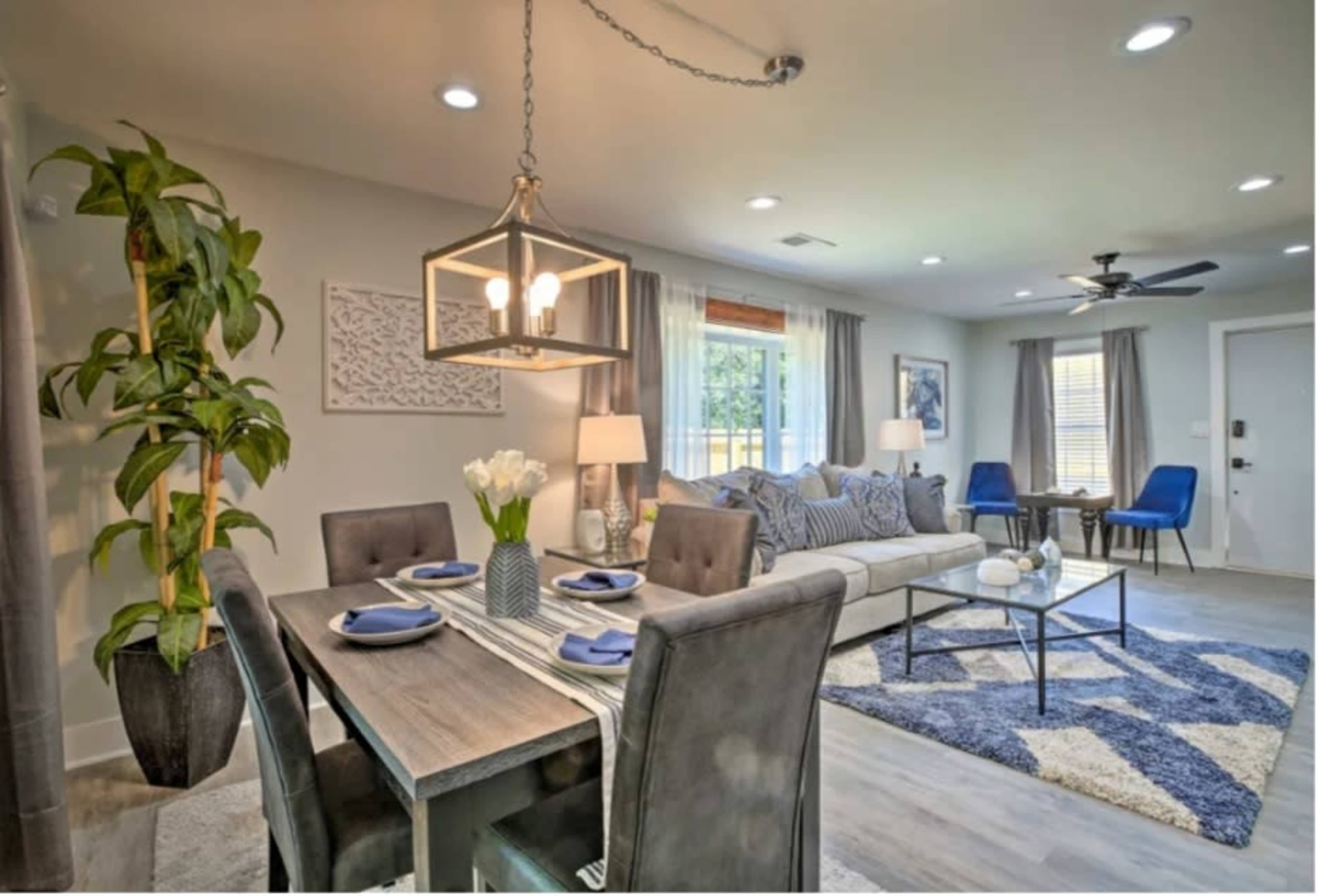A modern living and dining area featuring a grey sofa, a wooden dining table set for four, and decorative plants.