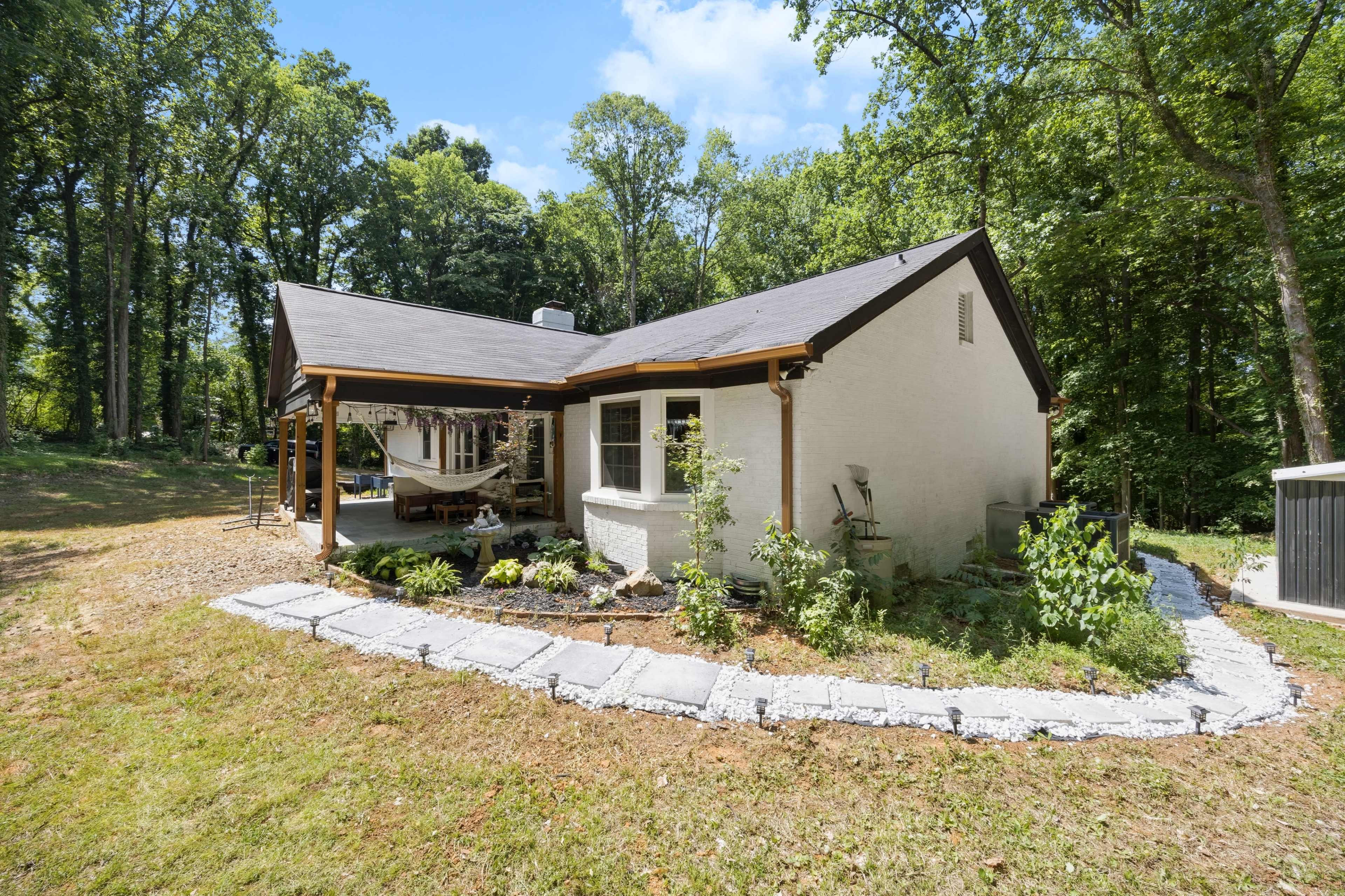 A single-story house with a porch surrounded by a landscaped yard, situated among tall trees.