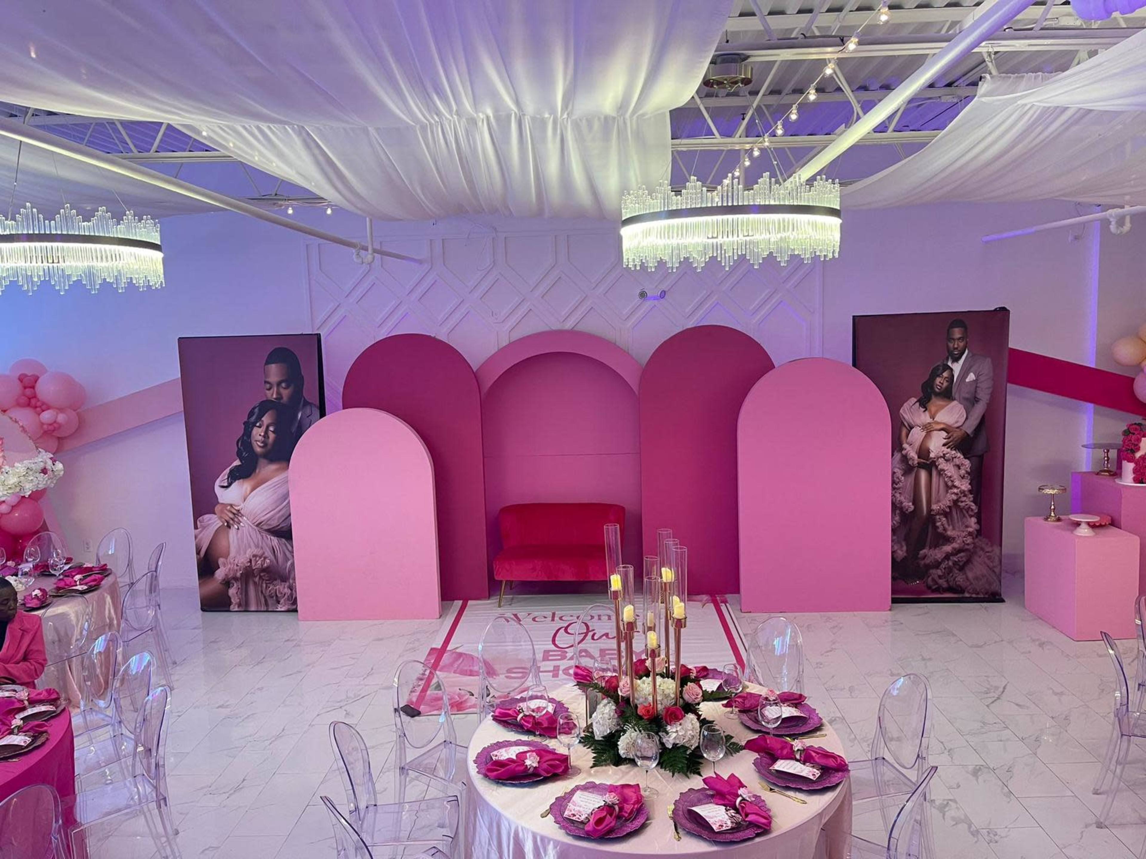 A decorated event space with pink arches, a velvet couch, and tables set with floral centerpieces for a celebration.