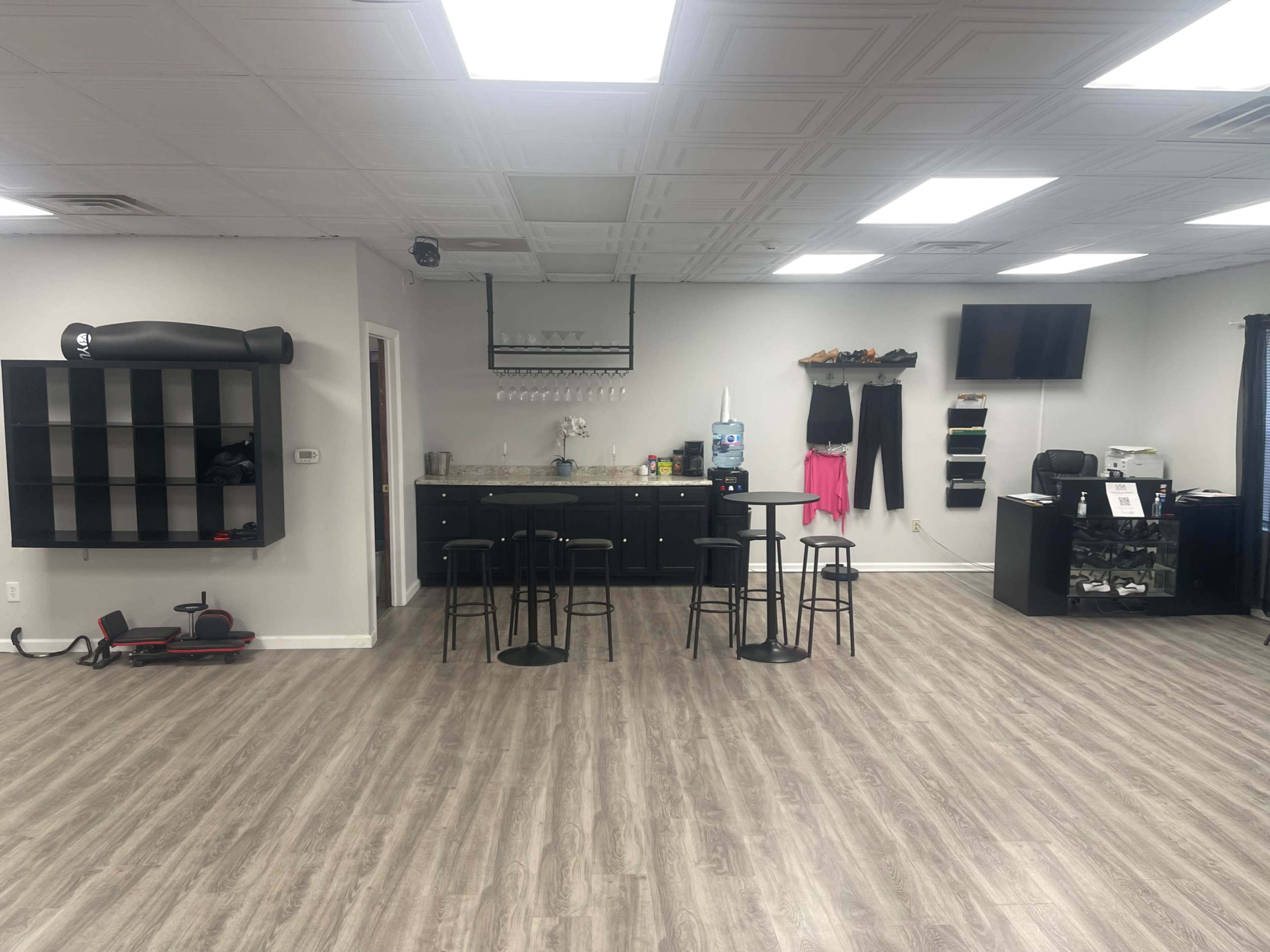 A spacious room with a dark cabinet, a table with four black chairs, and various fitness equipment, including a punching bag and a desk in the corner.