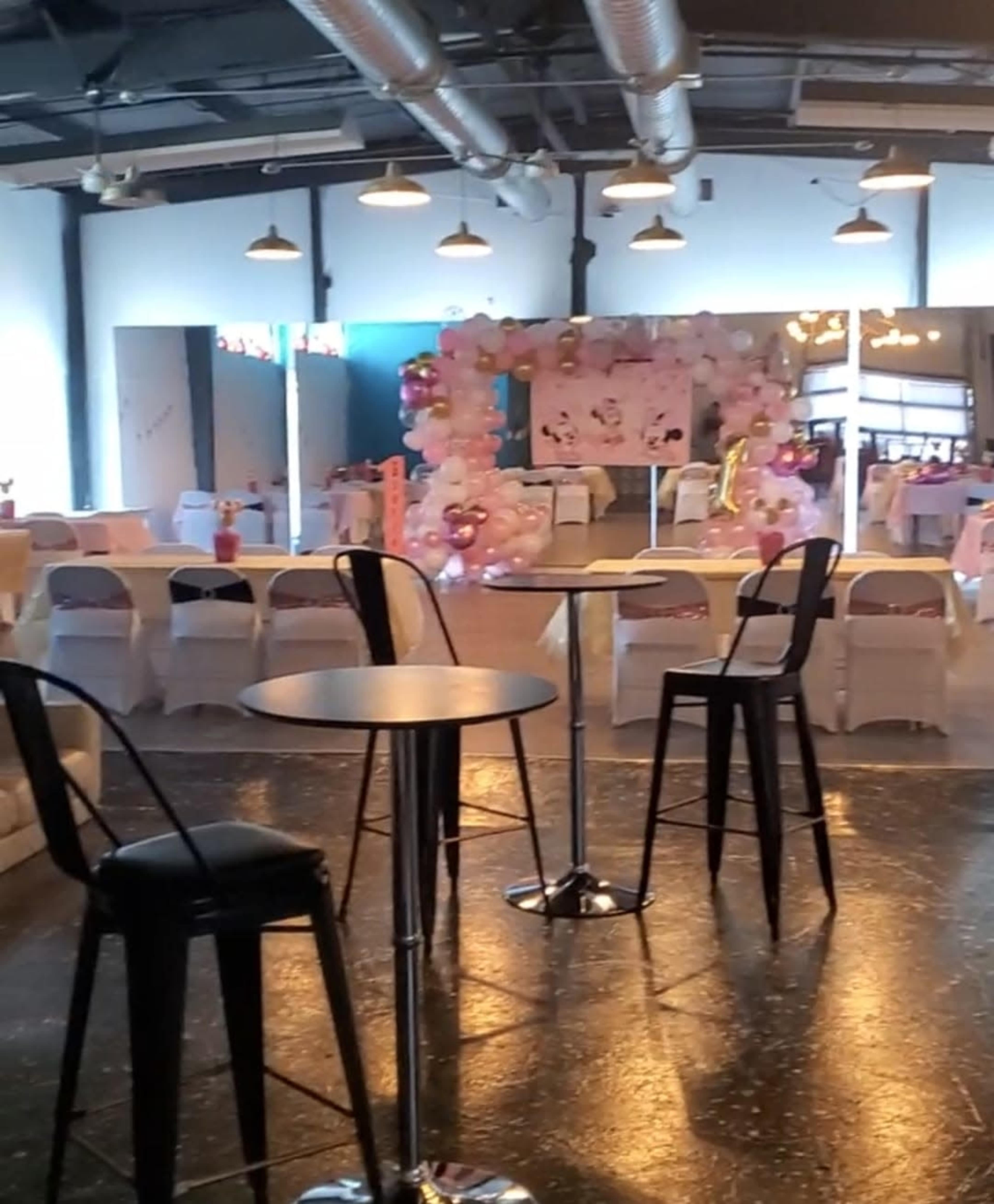 A spacious event venue set up with white chairs, tables, and a decorative arch made of balloons, ready for a celebration.