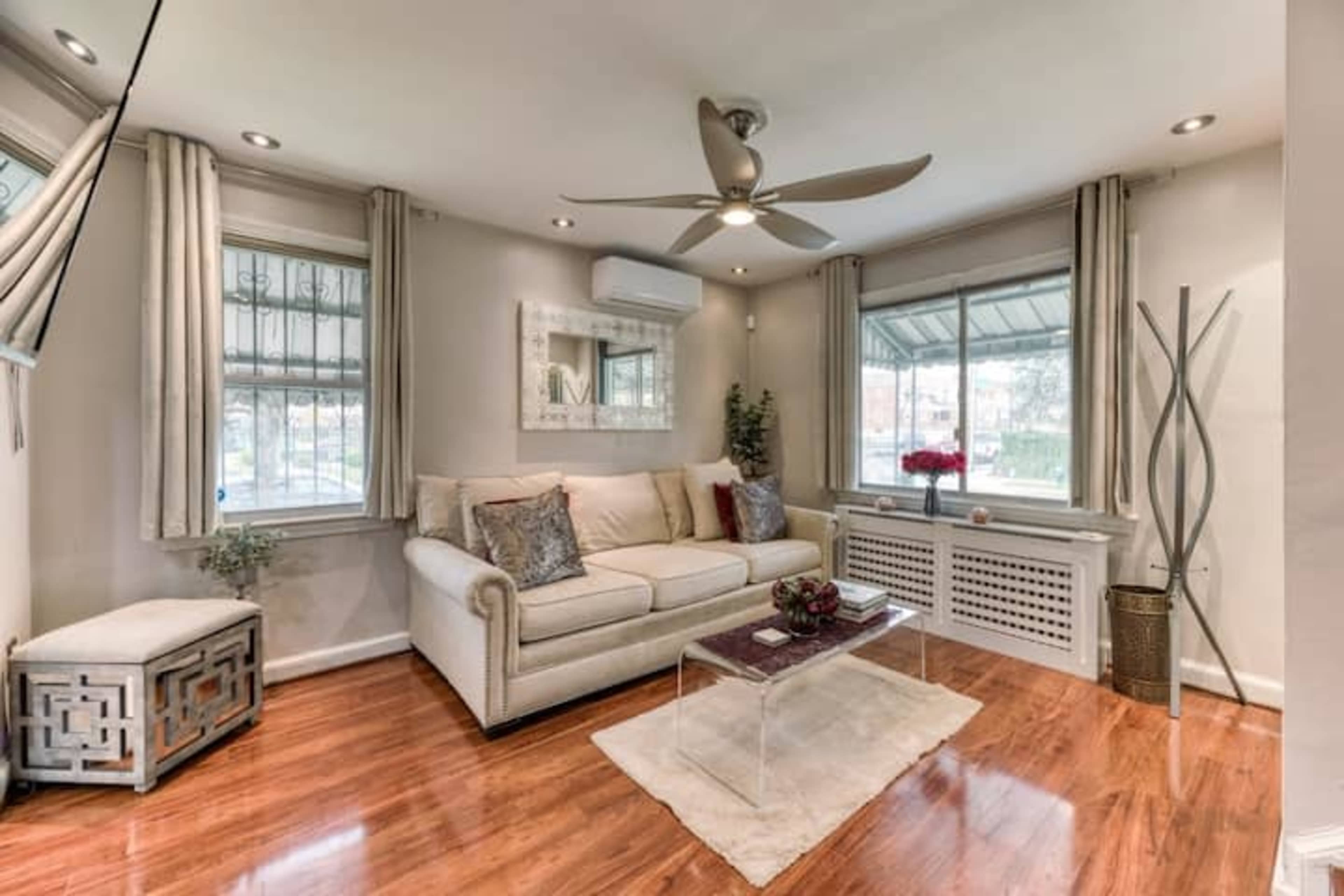 A living room with a beige sofa, a clear coffee table, and large windows allowing natural light to enter.