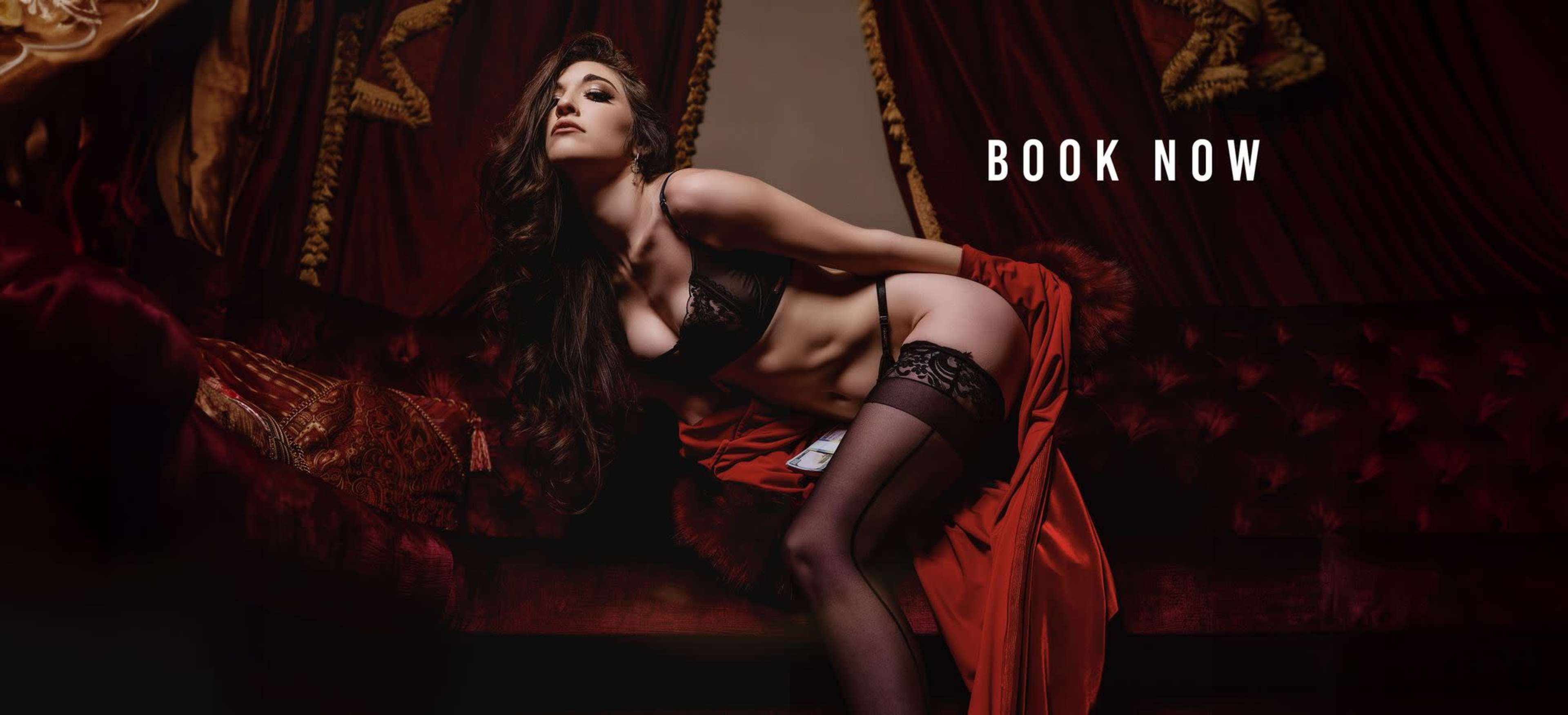 A woman in lingerie poses elegantly on a sofa, wearing a dramatic red robe.