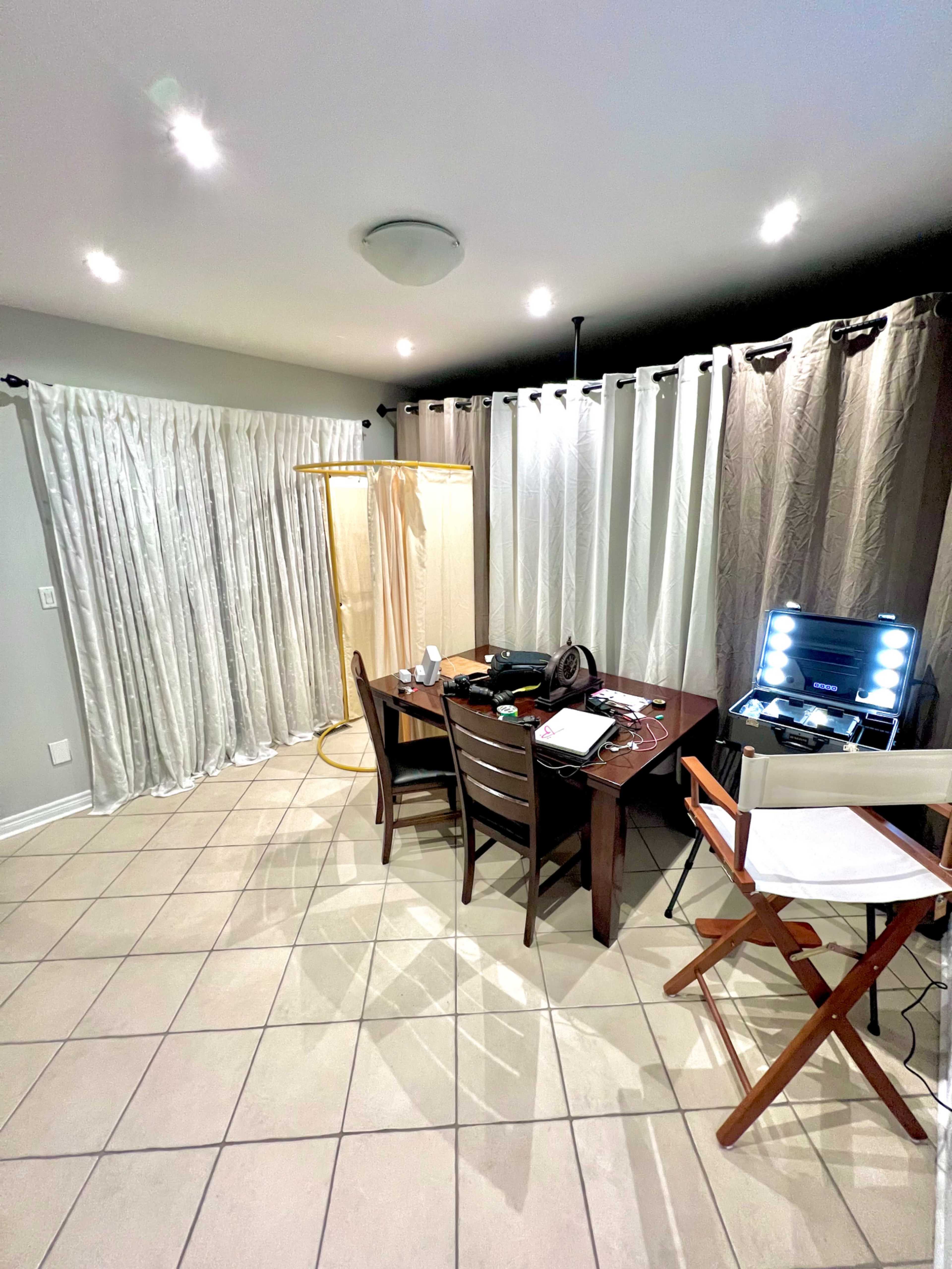 The image shows a room with a table and chairs, surrounded by curtains, a light source, and various equipment on the table.