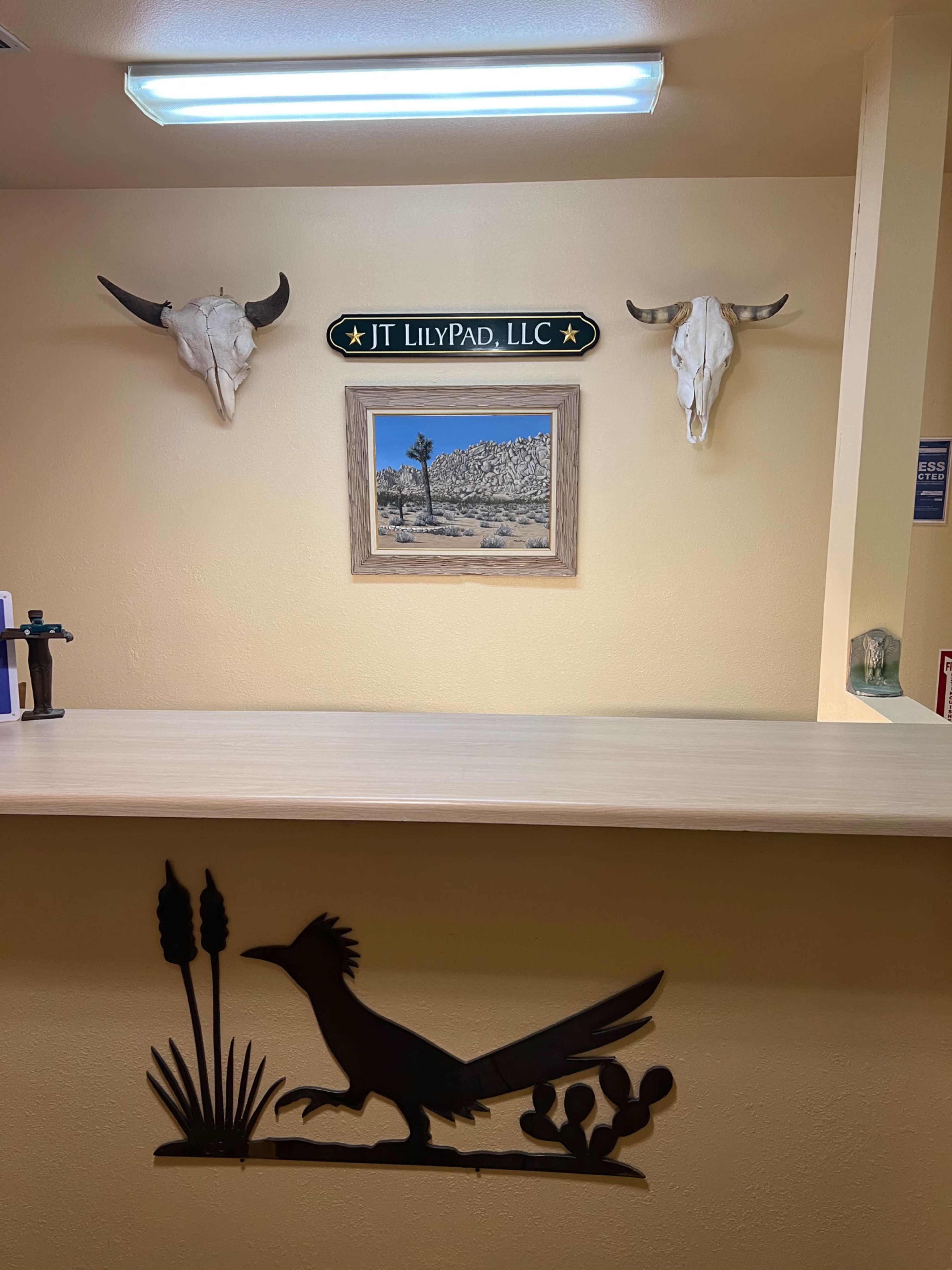 The image shows a reception desk with a sign reading "JT LILYPAD, LLC," flanked by two mounted animal skulls and a framed landscape painting on the wall behind.