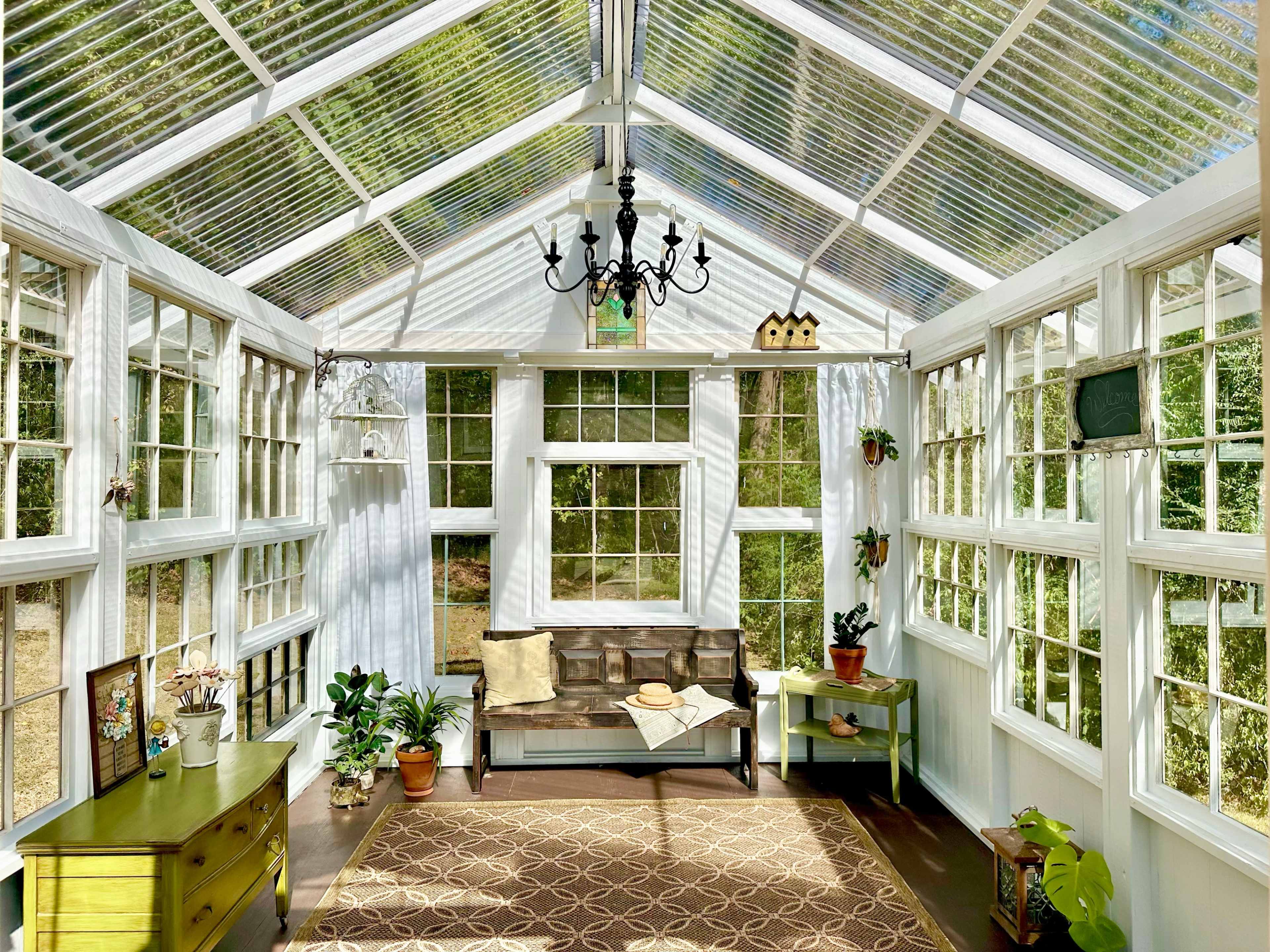 The image shows a bright sunroom with a wooden bench, potted plants, and large windows allowing natural light to fill the space.