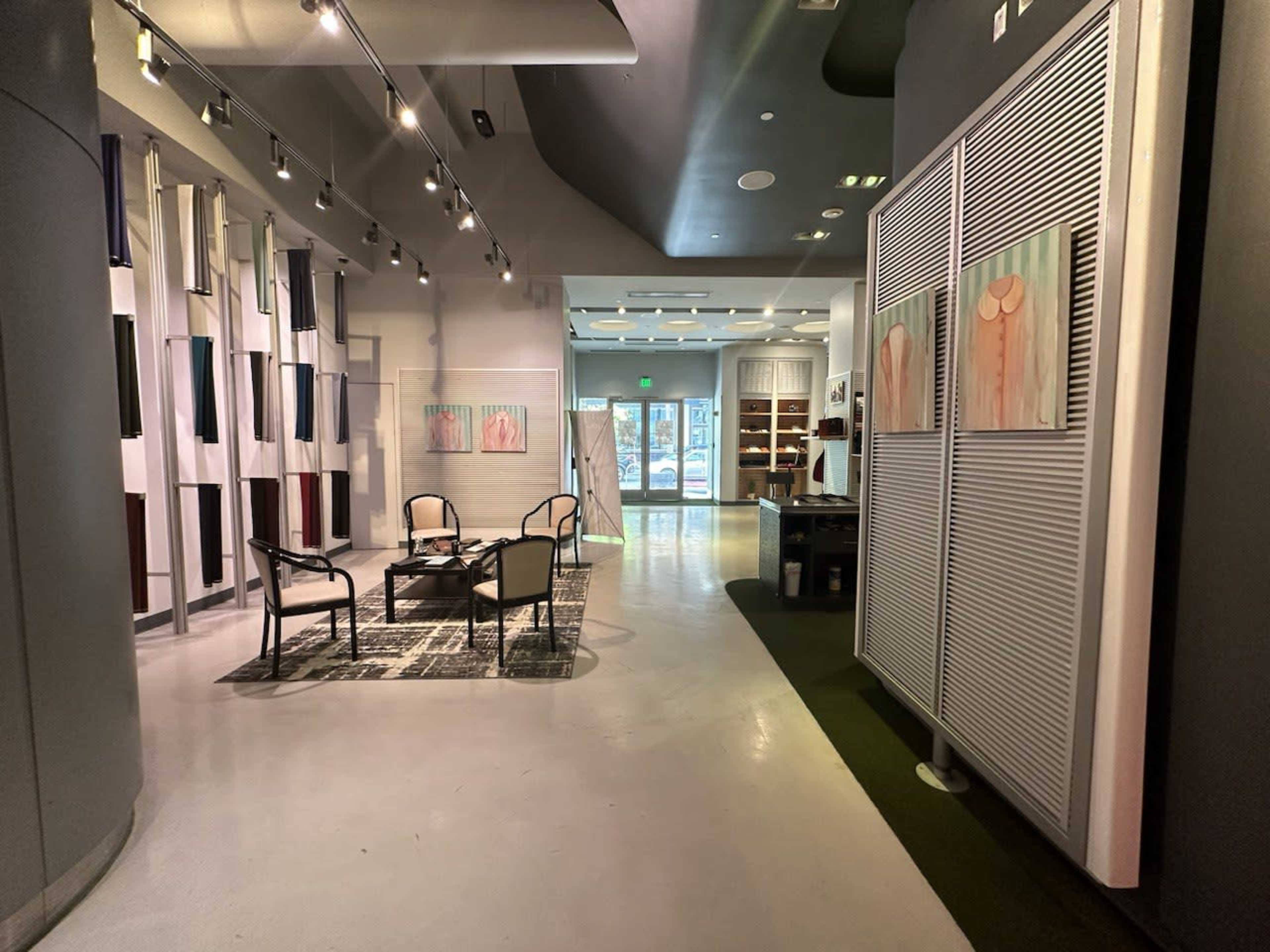 The image shows a modern interior space featuring a seating area with two chairs and a table, flanked by art on the walls and large windows offering natural light.