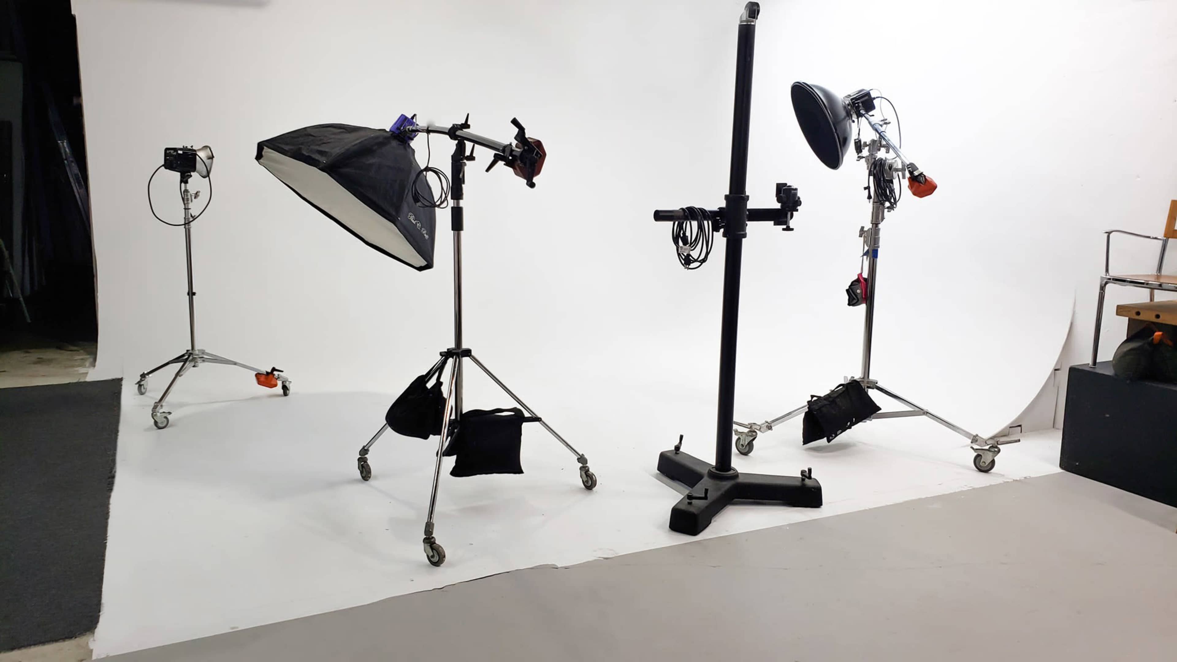 A photography studio setup with three light stands, each equipped with softboxes and reflectors, against a plain white backdrop.