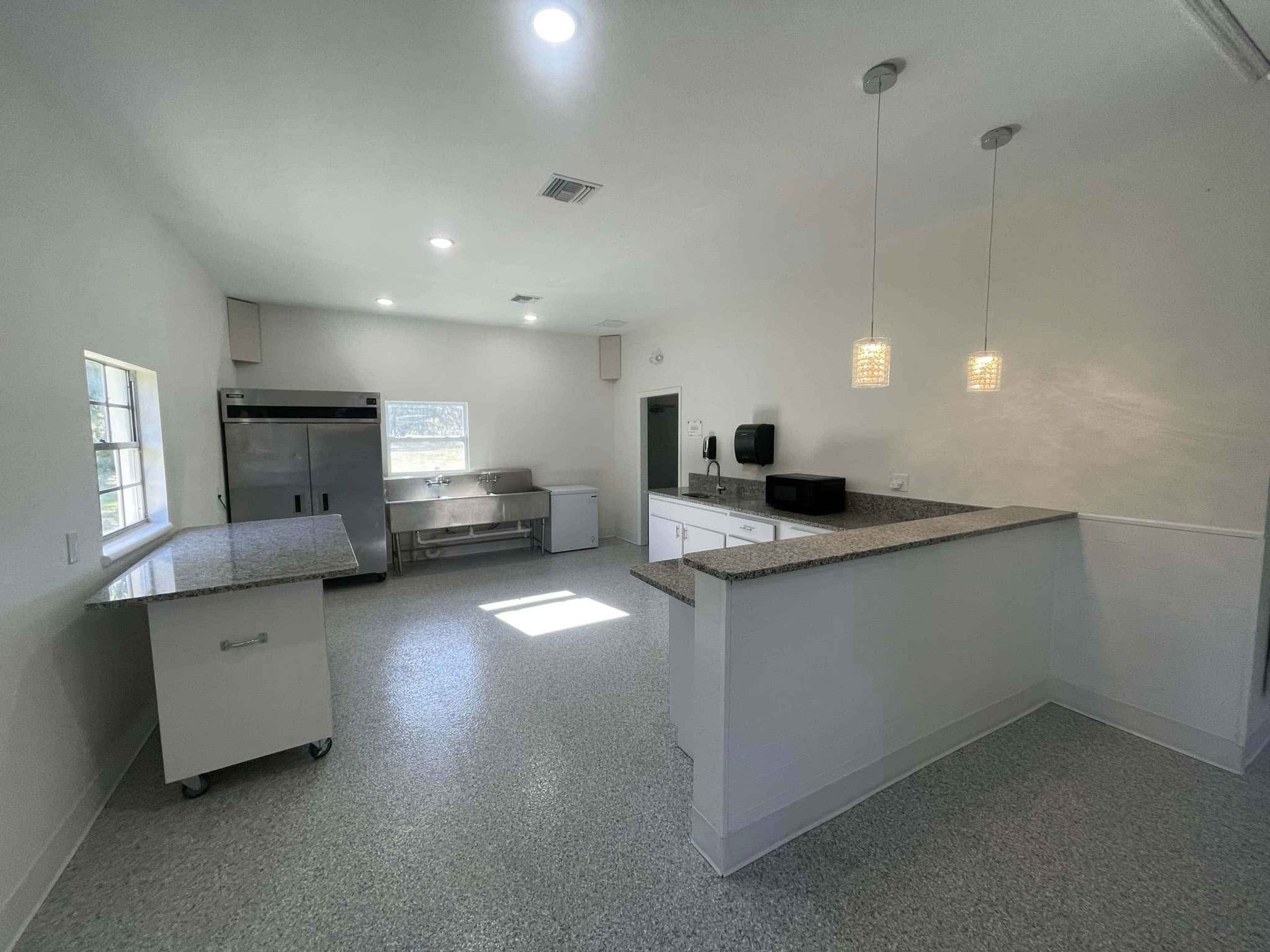 A modern kitchen with light-colored walls, a countertop with pendant lighting, a large stainless steel refrigerator, and an island on wheels.