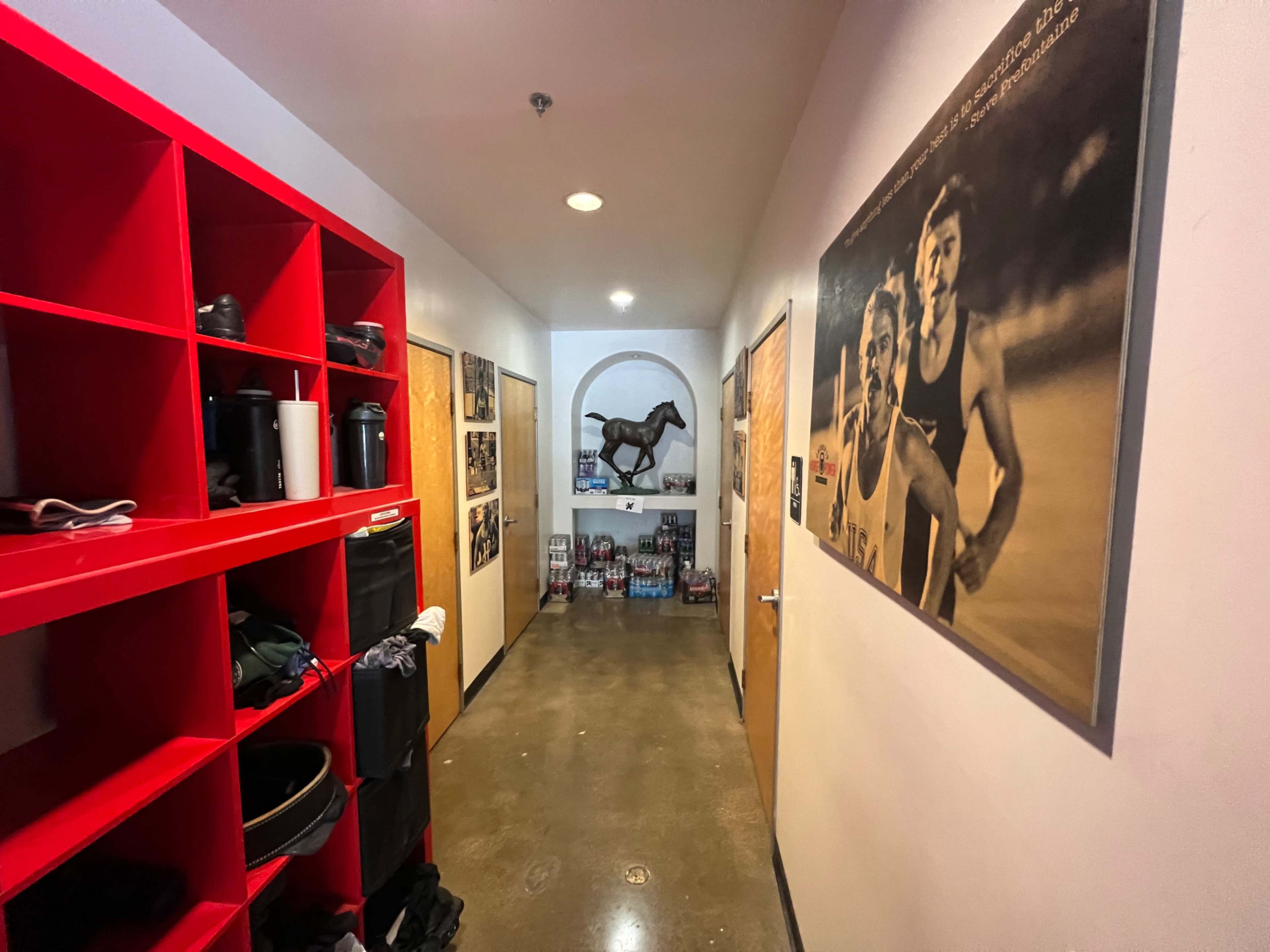 A long hallway features red shelving units on one side and black-and-white photographs on the walls, with a statue of a horse at the end.