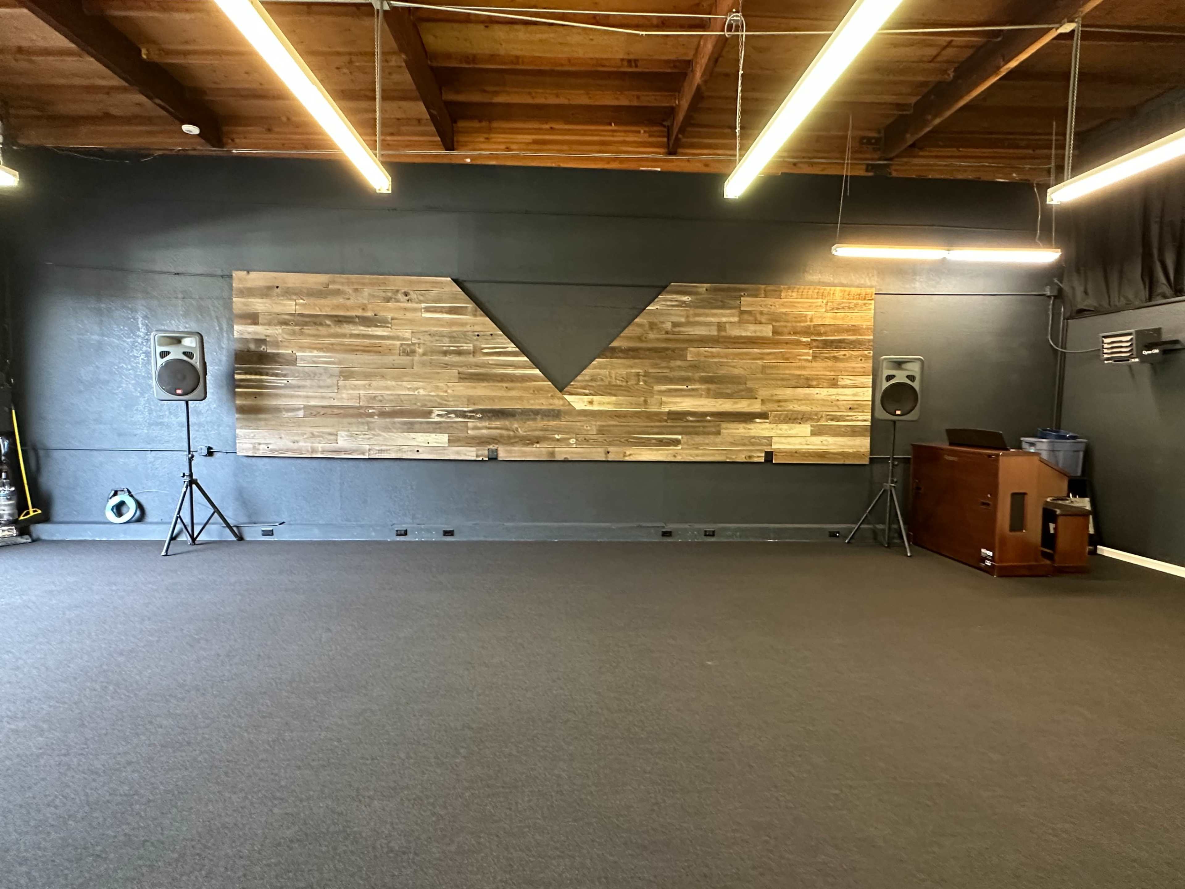 A spacious room with a wooden accent wall, two speakers on stands, and a wooden piano in the corner.