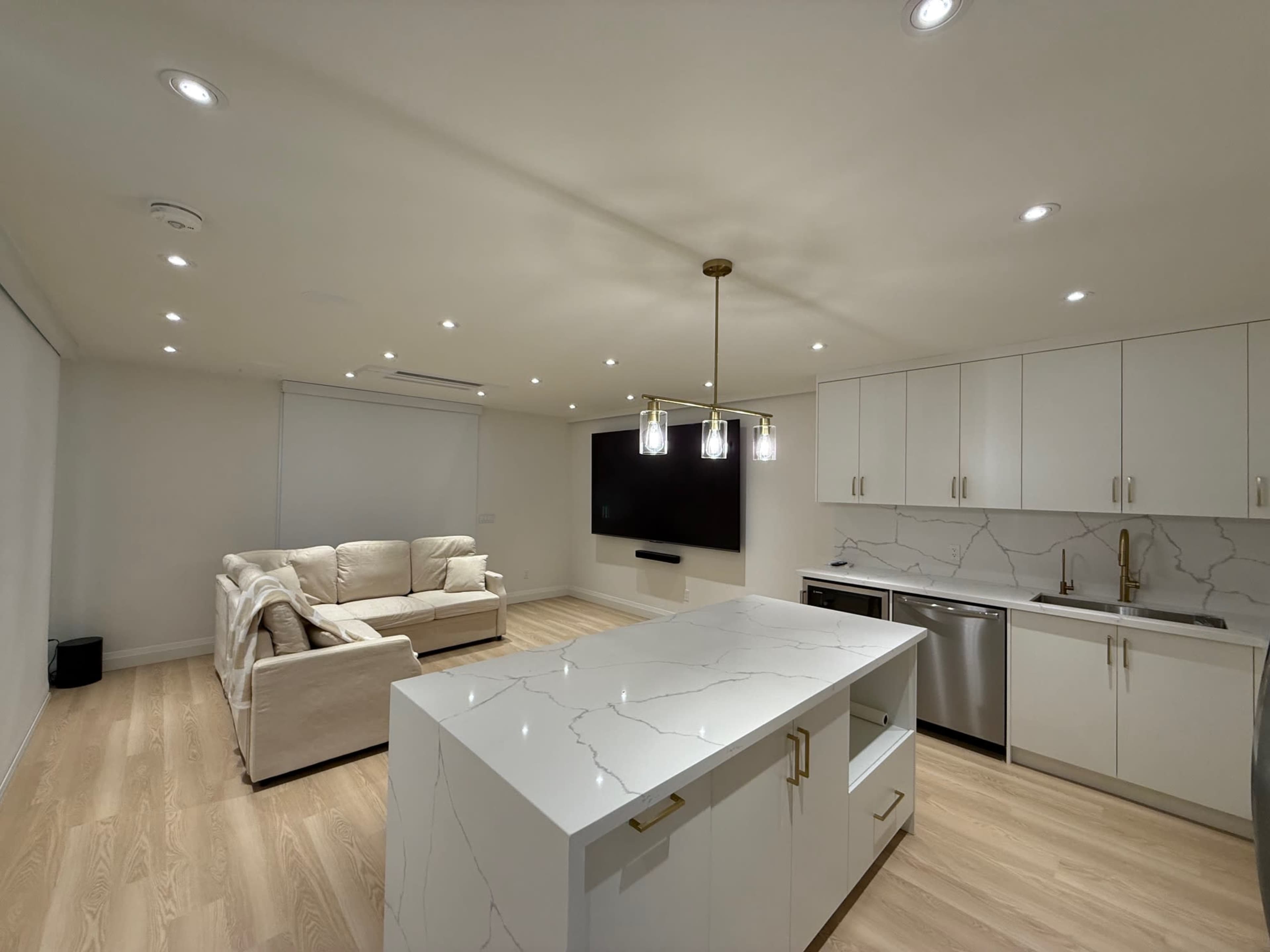 The image shows a modern kitchen and living area featuring a white marble island, stainless steel appliances, and a cream-colored couch.