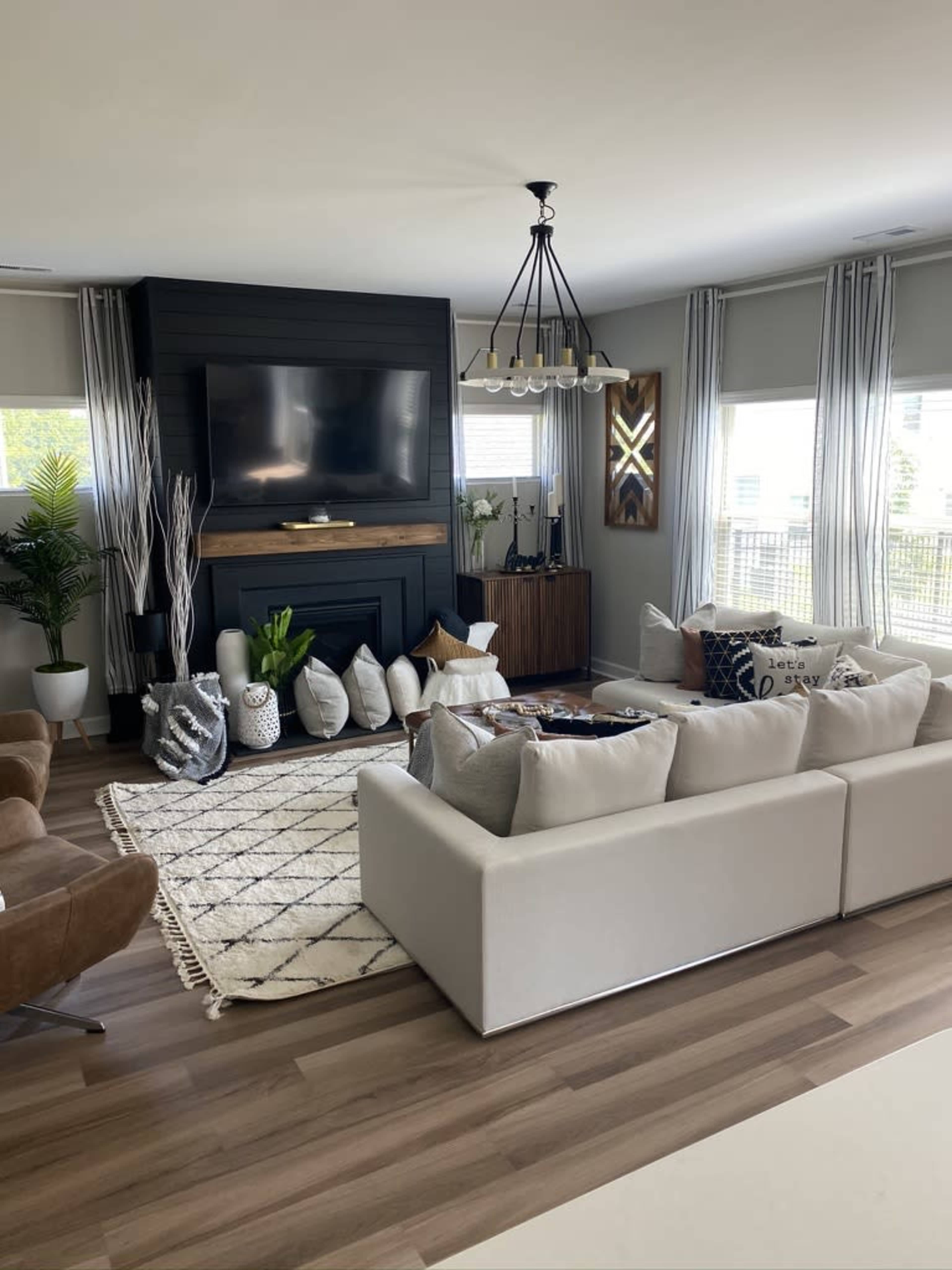 A modern living room features a white sectional sofa, a large flat-screen TV mounted above a black fireplace, and decorative pillows arranged on a patterned rug.