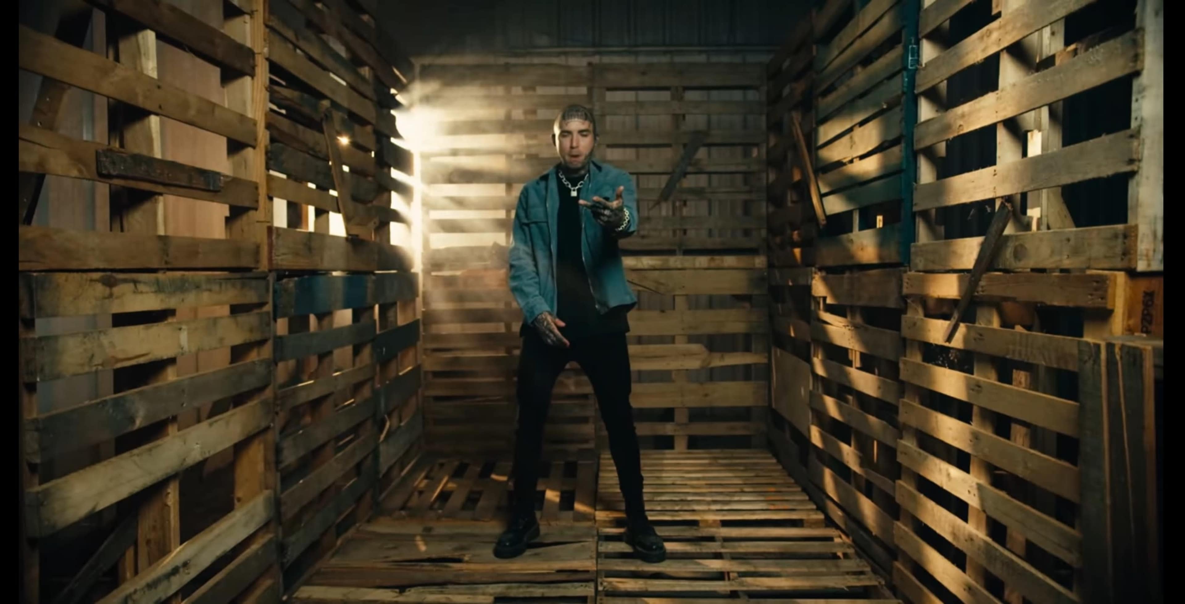 A person stands in a wooden structure made of pallets, with light streaming in from one side.