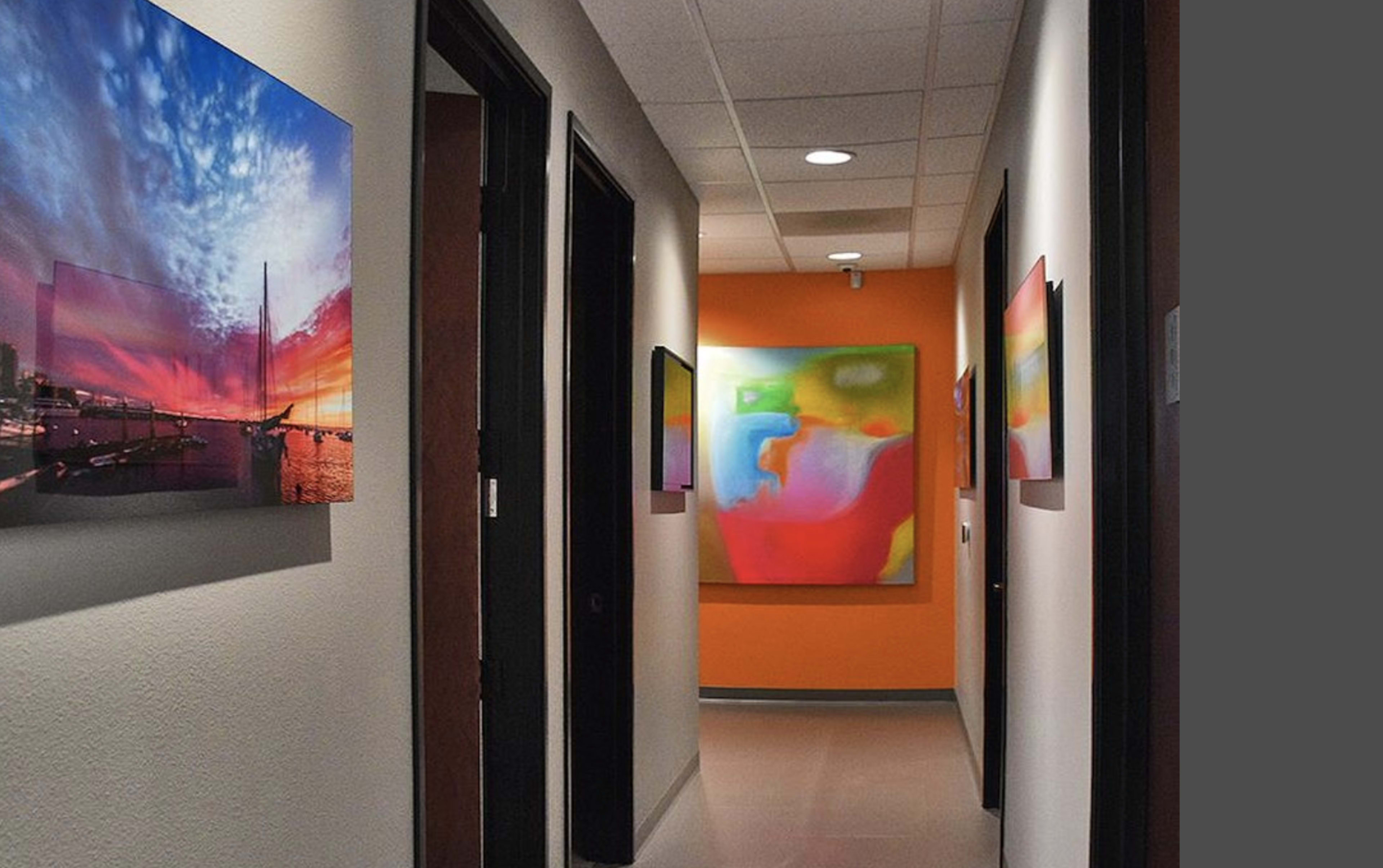A hallway with colorful artwork displayed on the walls, leading to an orange-colored accent wall.