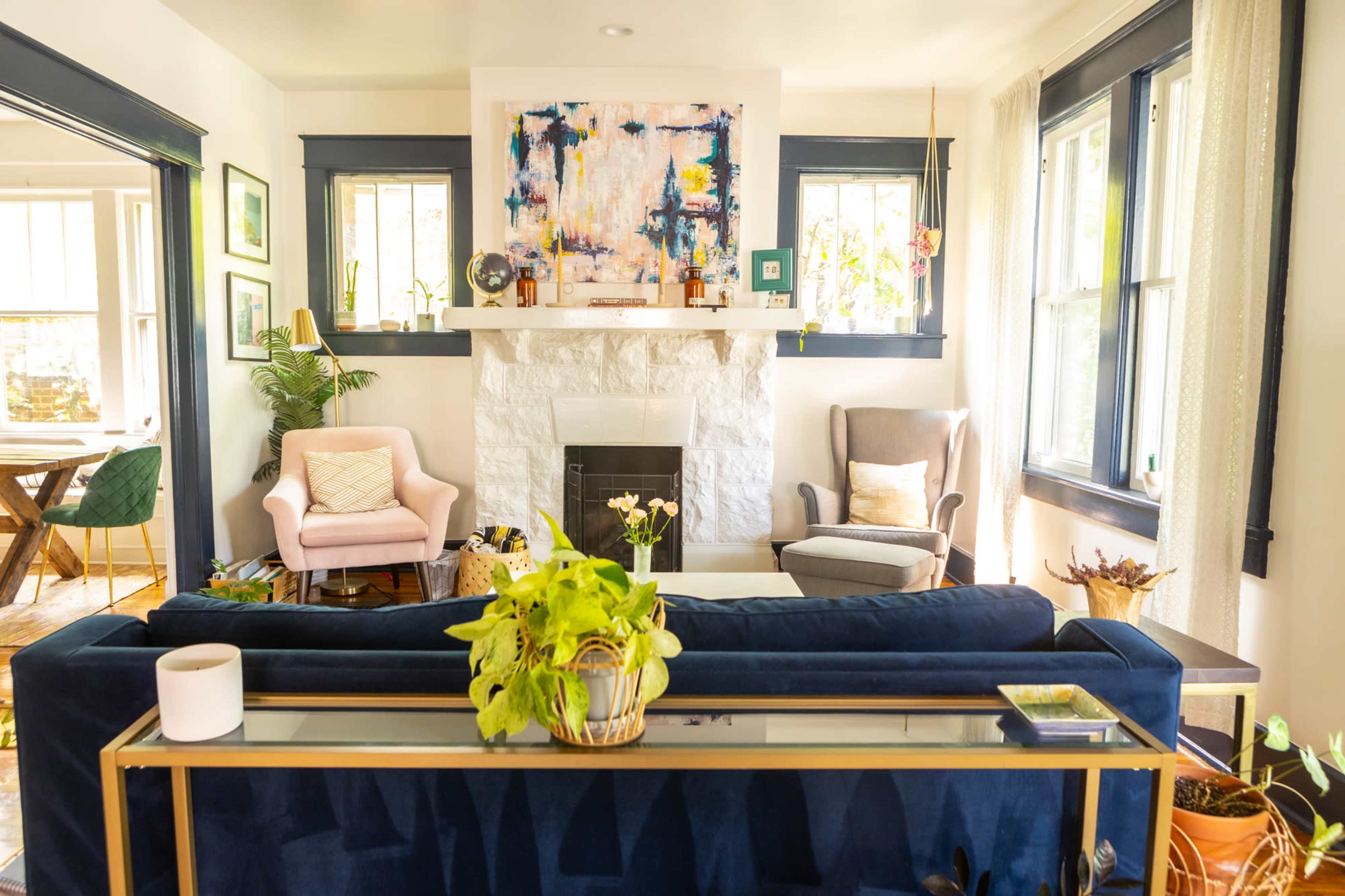 A bright living room featuring a navy blue sofa, two armchairs, a white stone fireplace, and colorful artwork above the mantel.