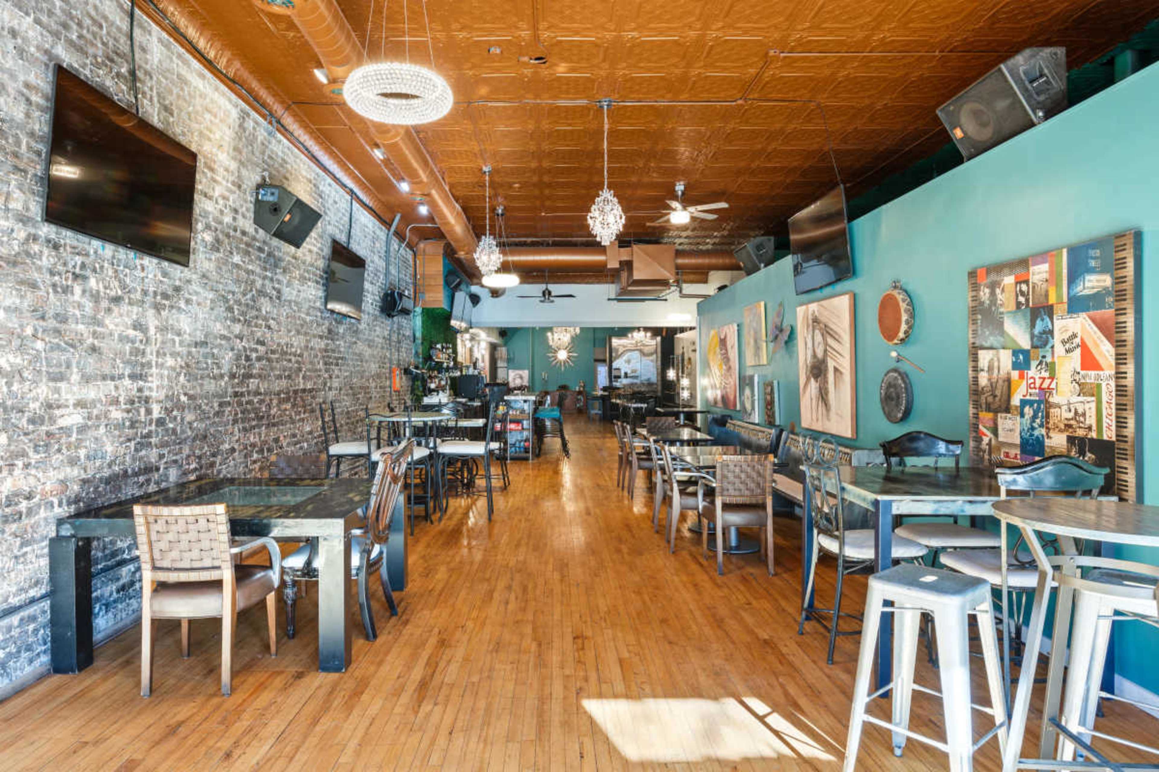 The image shows a spacious restaurant interior with wooden floors, exposed brick walls, and tables arranged throughout the room.