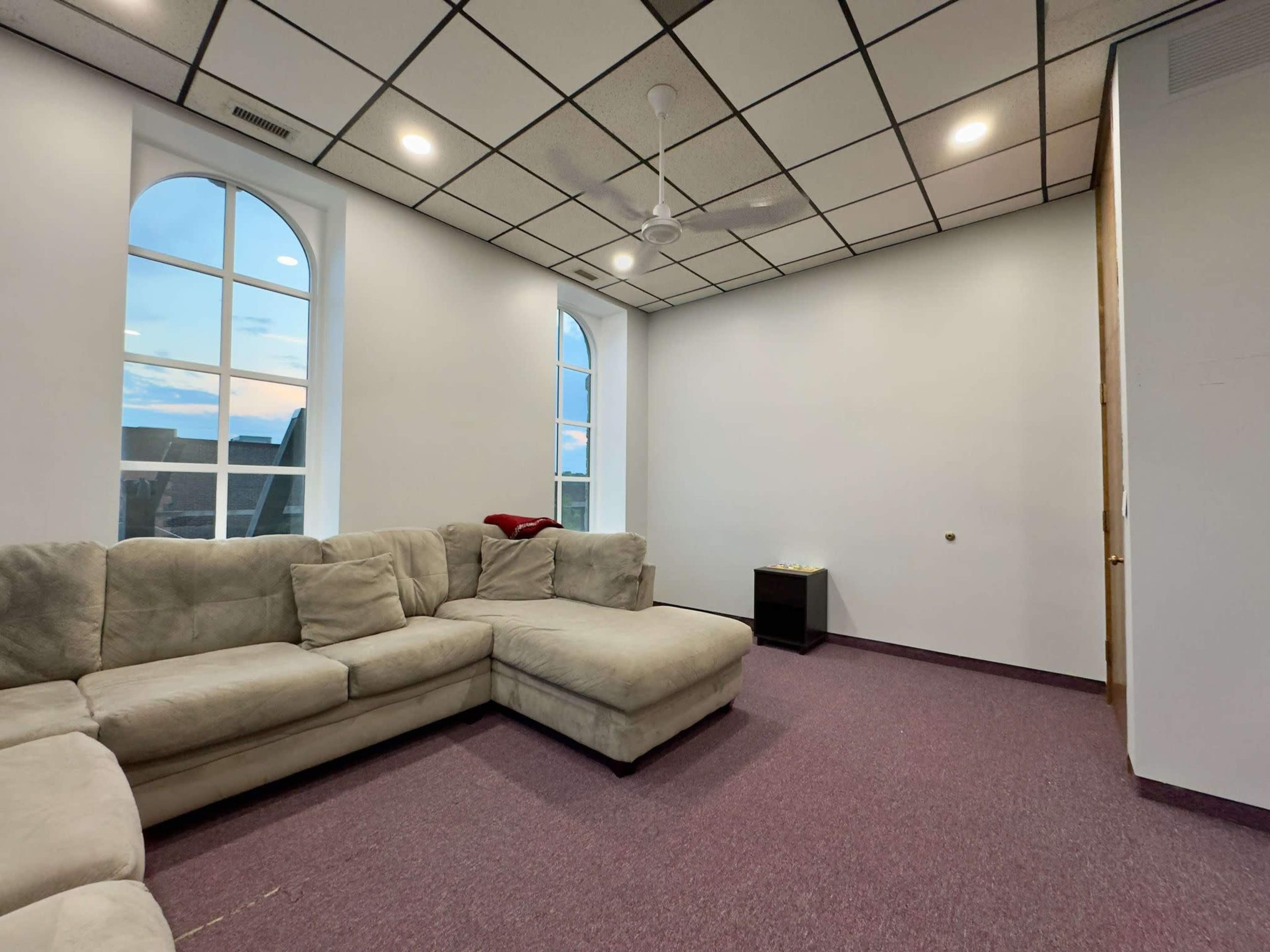 A spacious room features a large sectional sofa, purple carpet, and windows with arches.