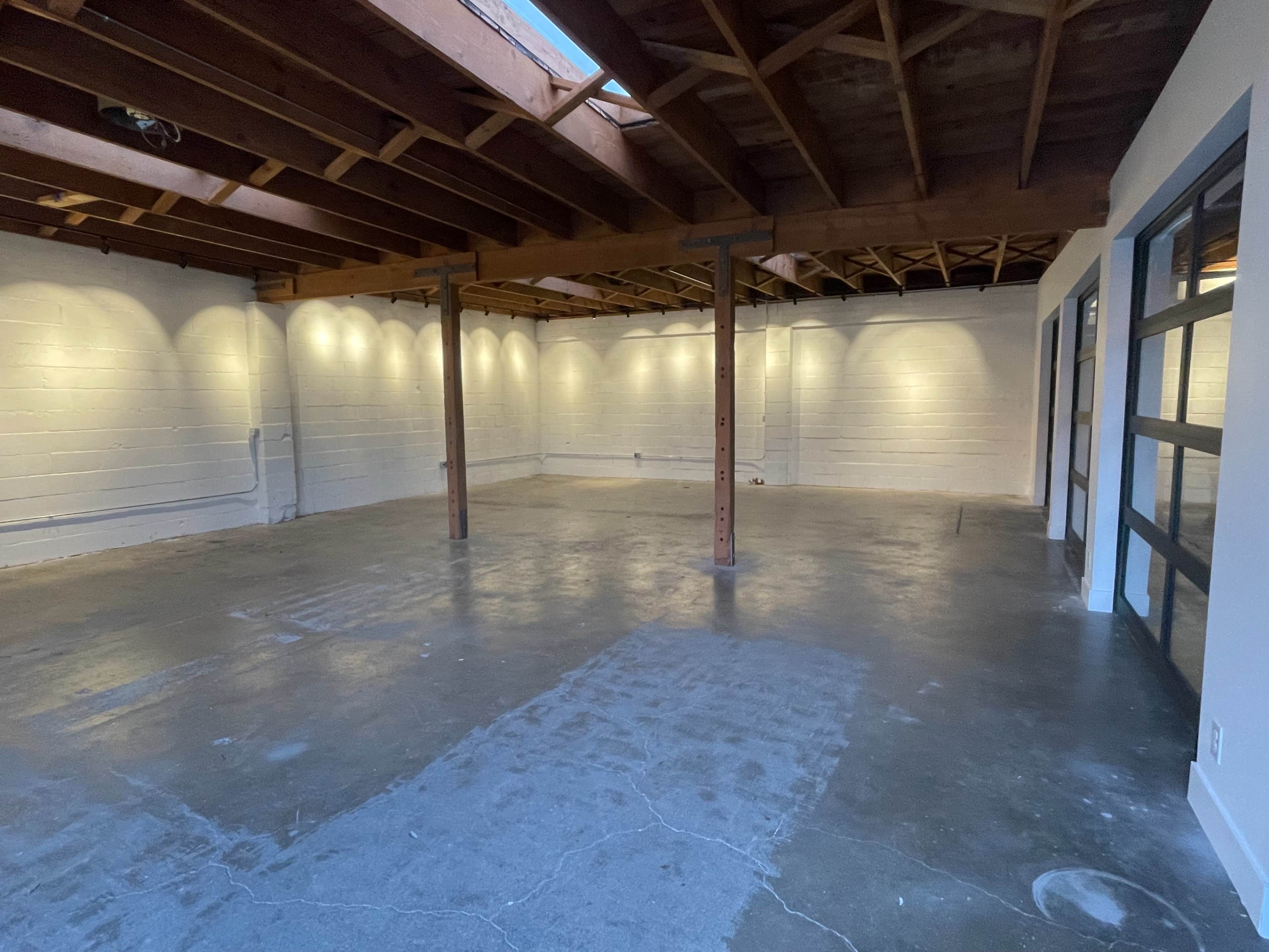 A spacious, empty interior room with exposed wooden beams and concrete flooring.