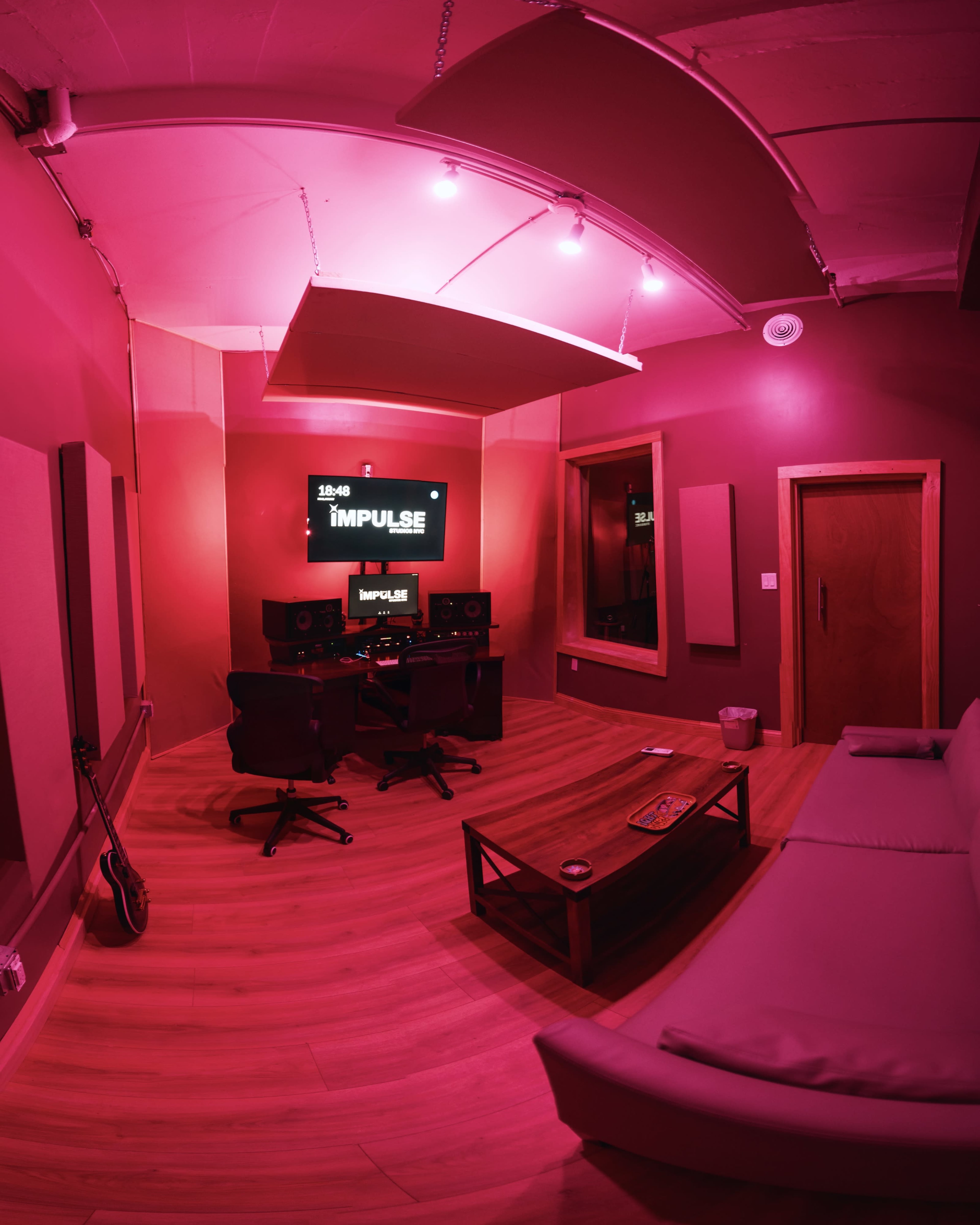 A music studio featuring a soundboard, two chairs, a couch, and pink lighting.