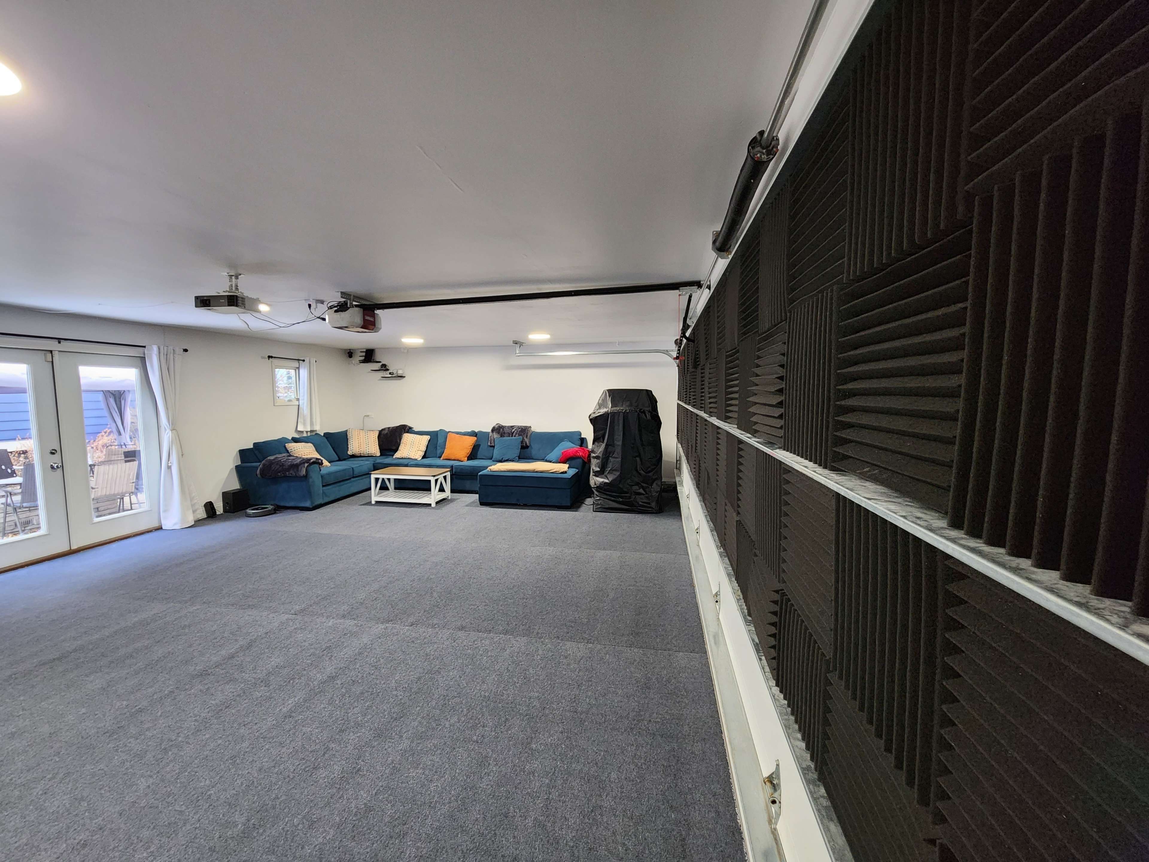 A spacious room with gray carpeting, a seating area featuring a dark blue couch and a white coffee table, and an acoustic panelled wall.