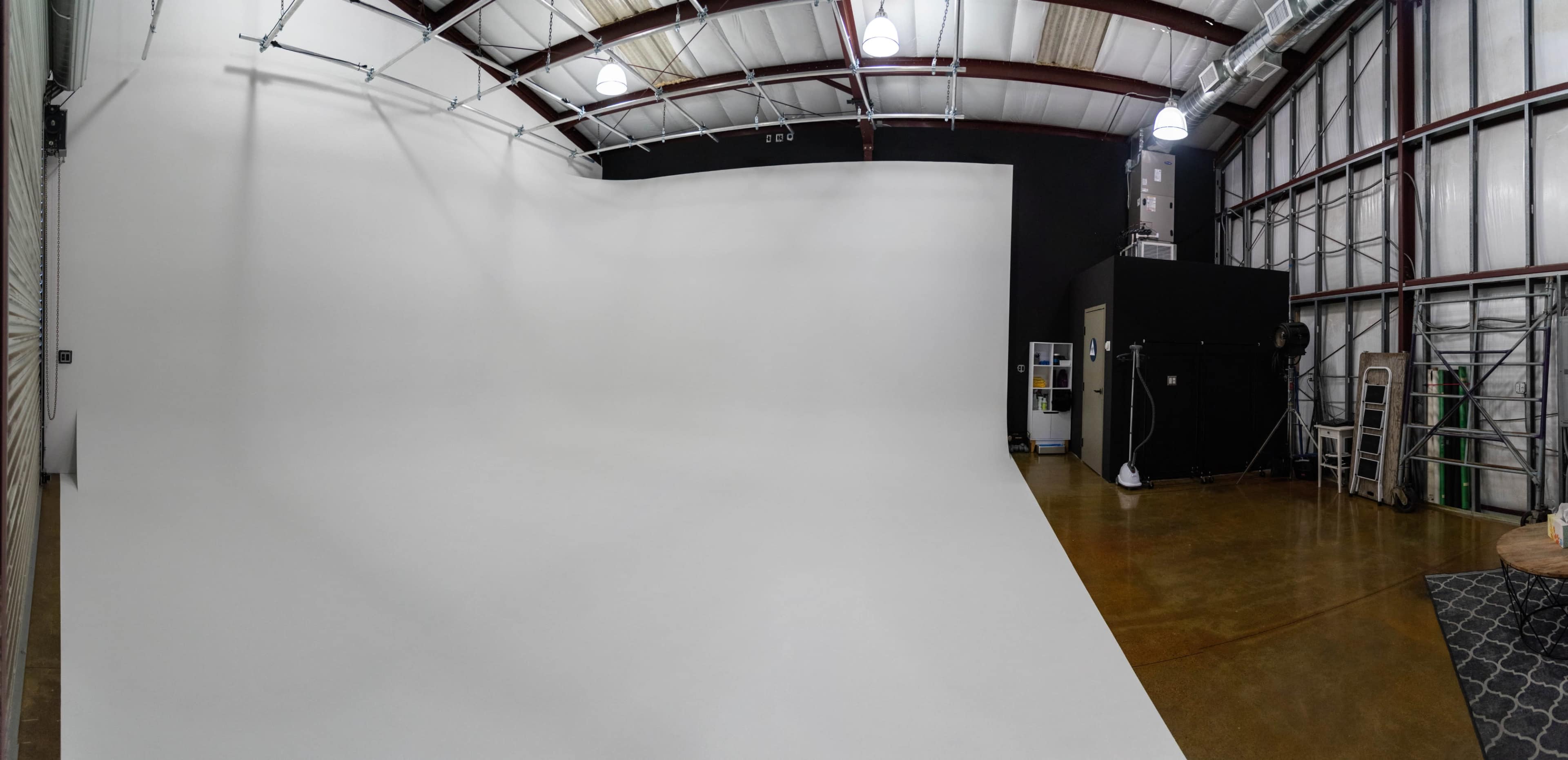 A spacious photography studio featuring a large white backdrop, smooth floor, and various studio equipment along the walls.