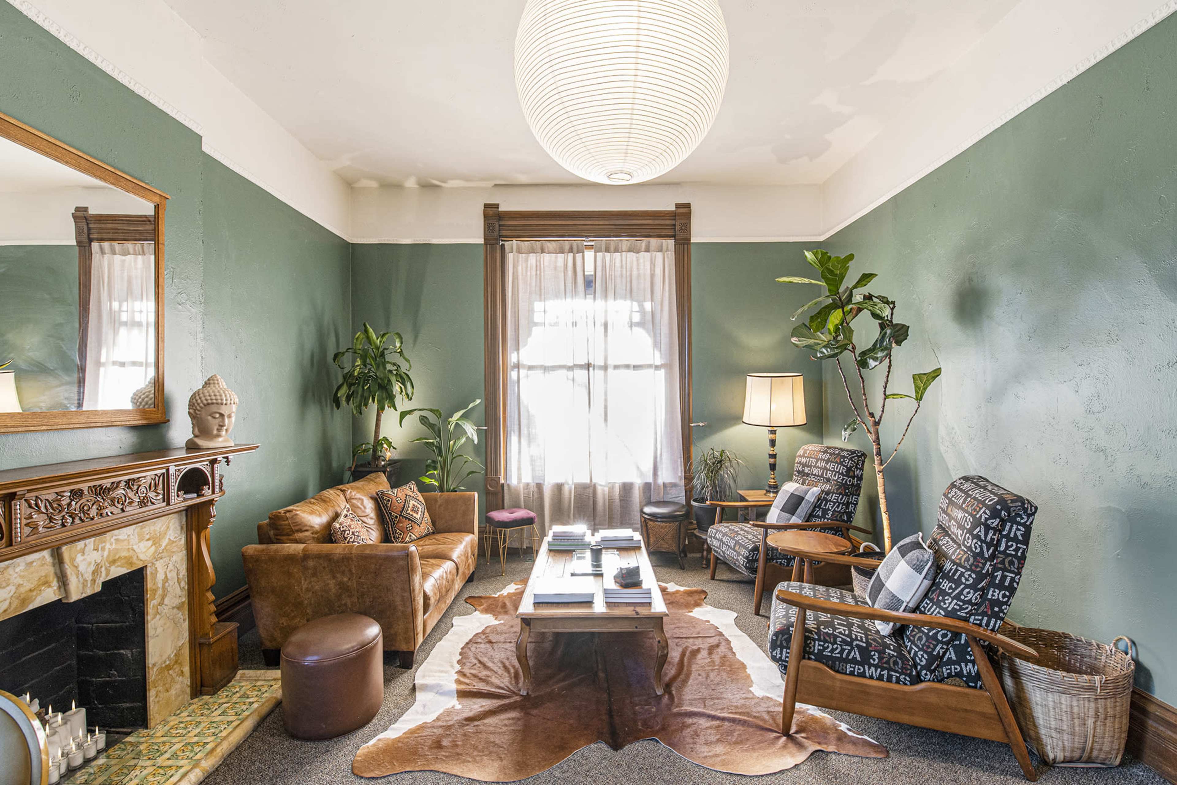 The living room features a green wall, a mix of vintage furniture, a large round pendant light, and decorative plants.
