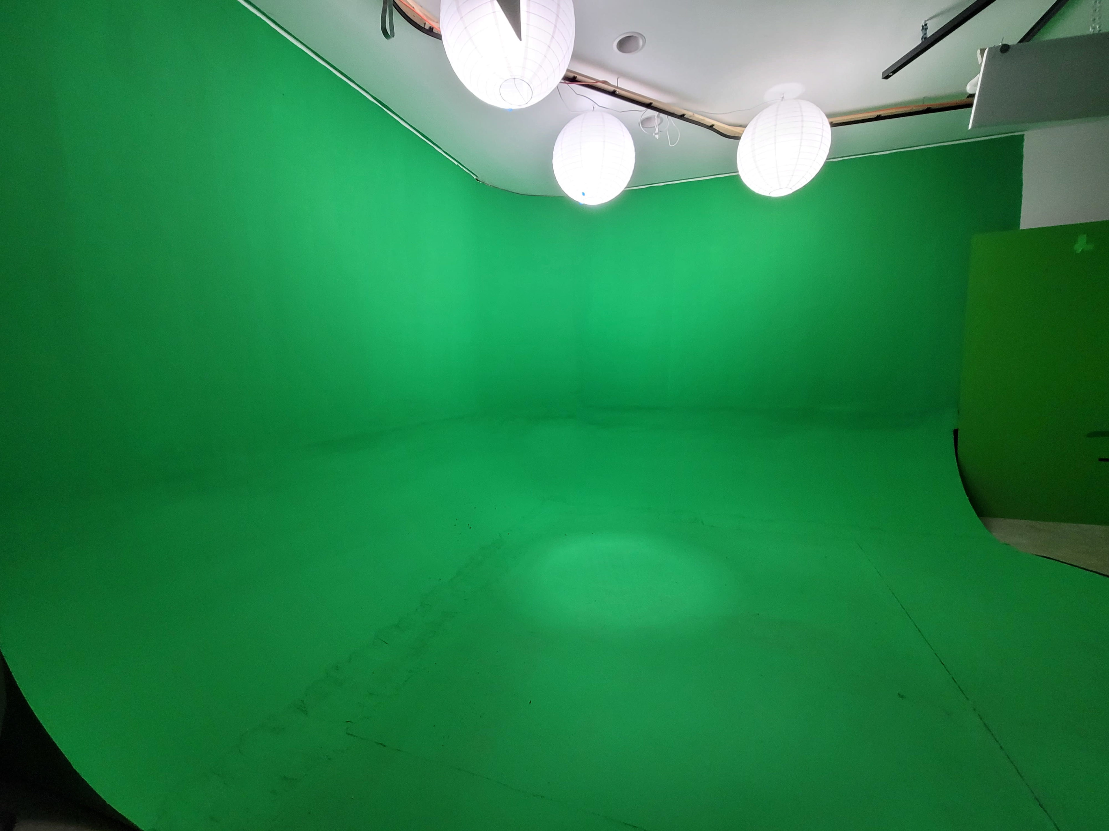 The image shows a studio space with a green screen backdrop and several hanging light fixtures.