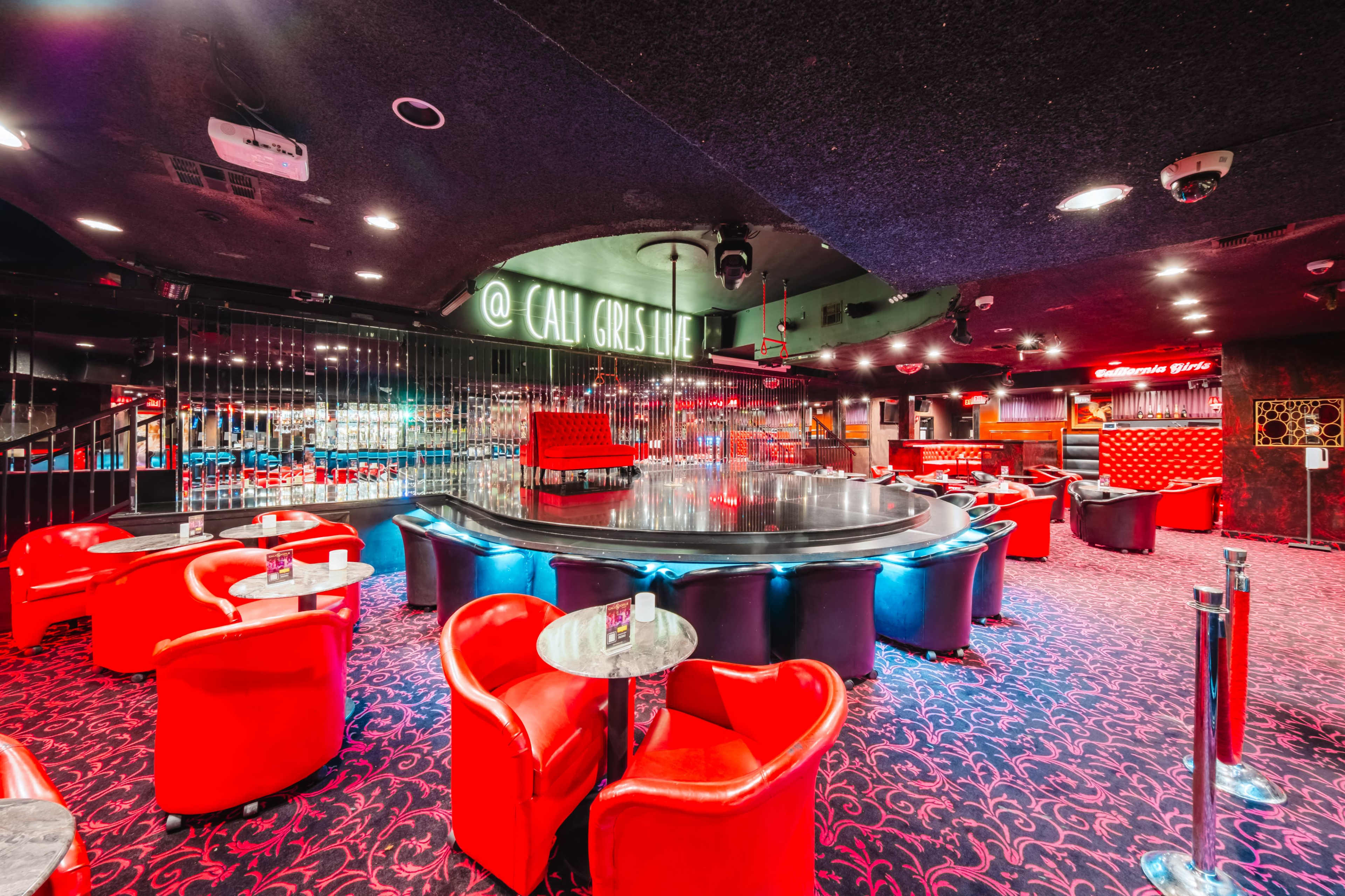 The image shows a dimly lit nightclub interior featuring red upholstered seating and a circular stage with a mirrored surface.