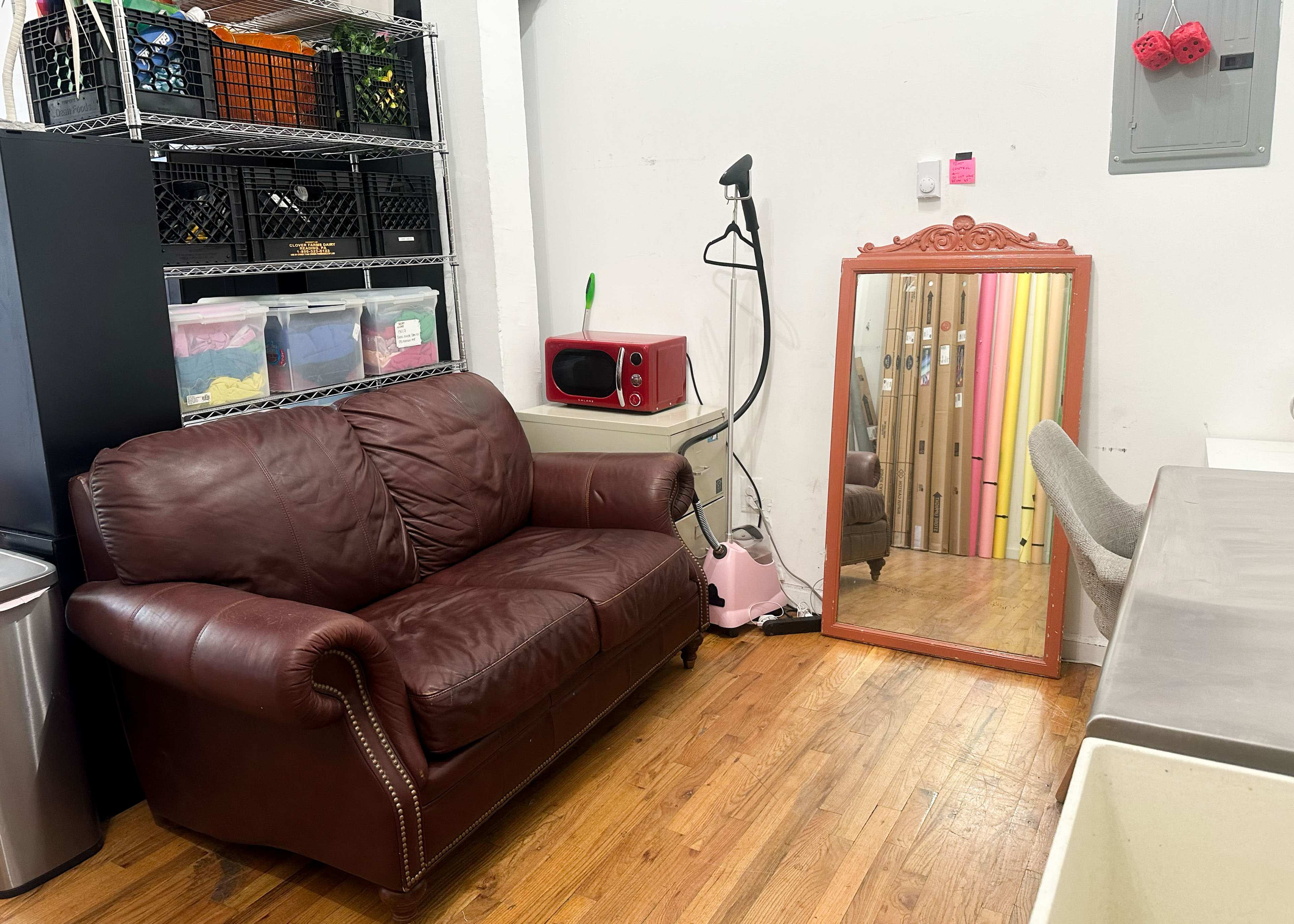 A brown leather sofa next to a large mirror, with a shelf containing storage bins and a microwave in the background.