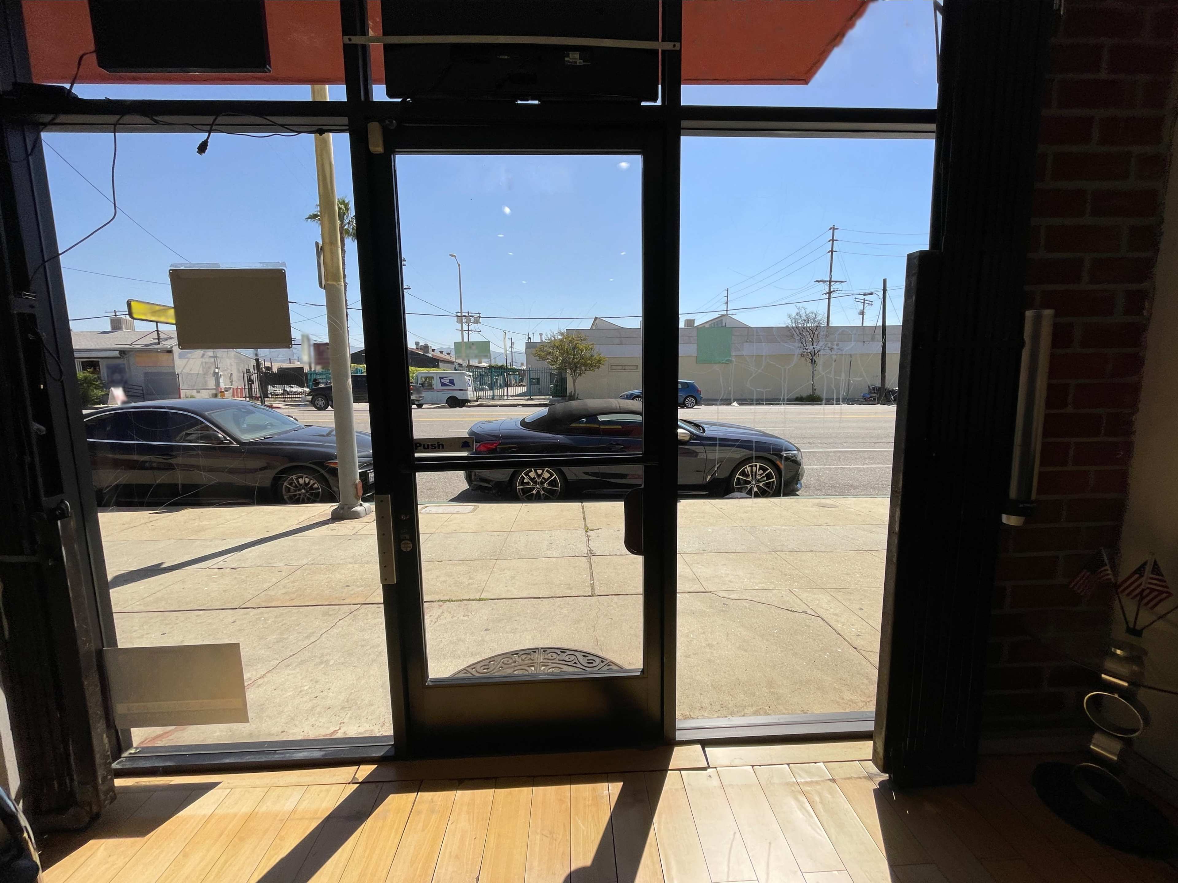 The image shows a storefront entrance with a view of a street, featuring parked cars and clear blue skies.