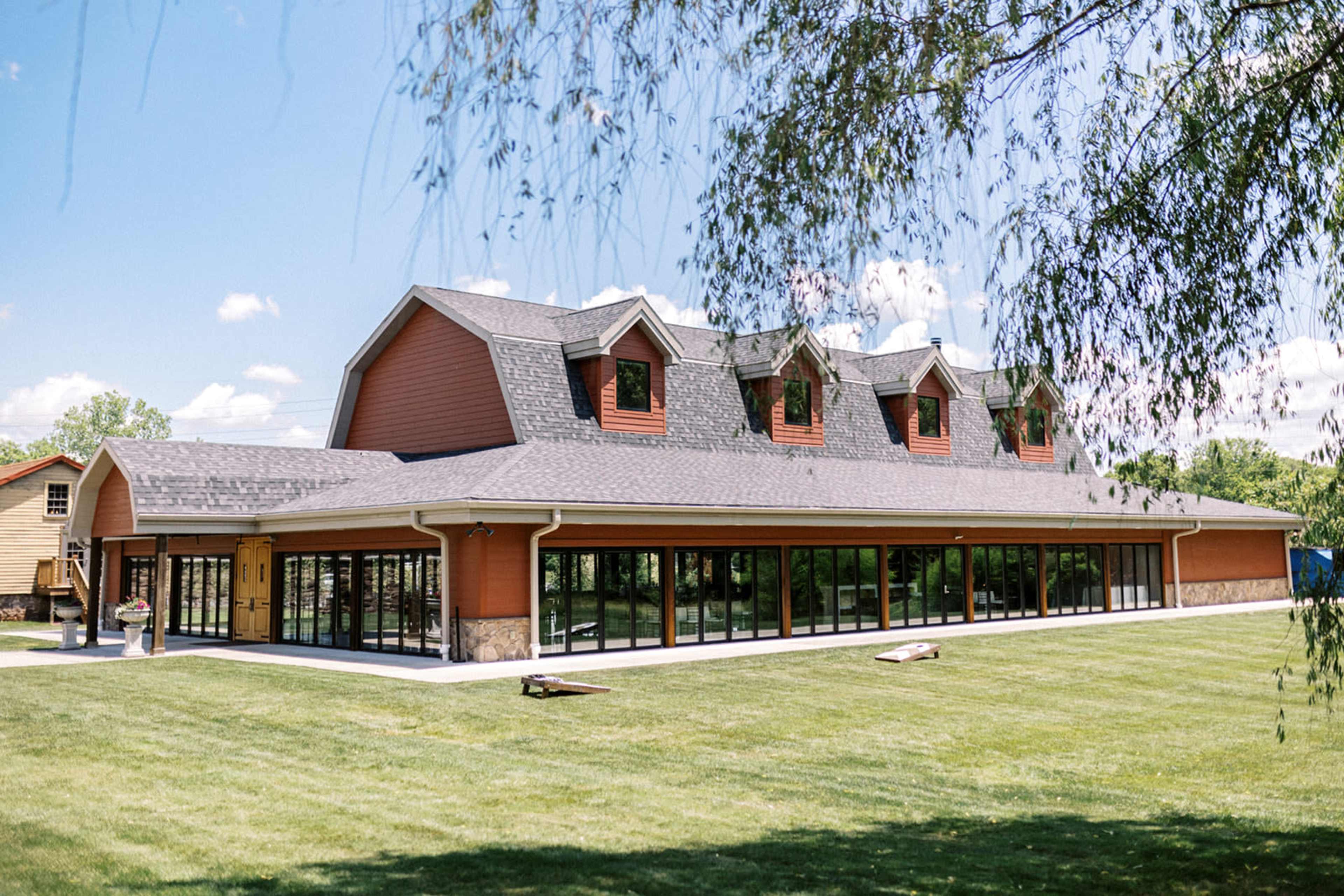 A large, modern building with multiple peaked roofs and extensive glass windows, situated on a grassy area under a blue sky.
