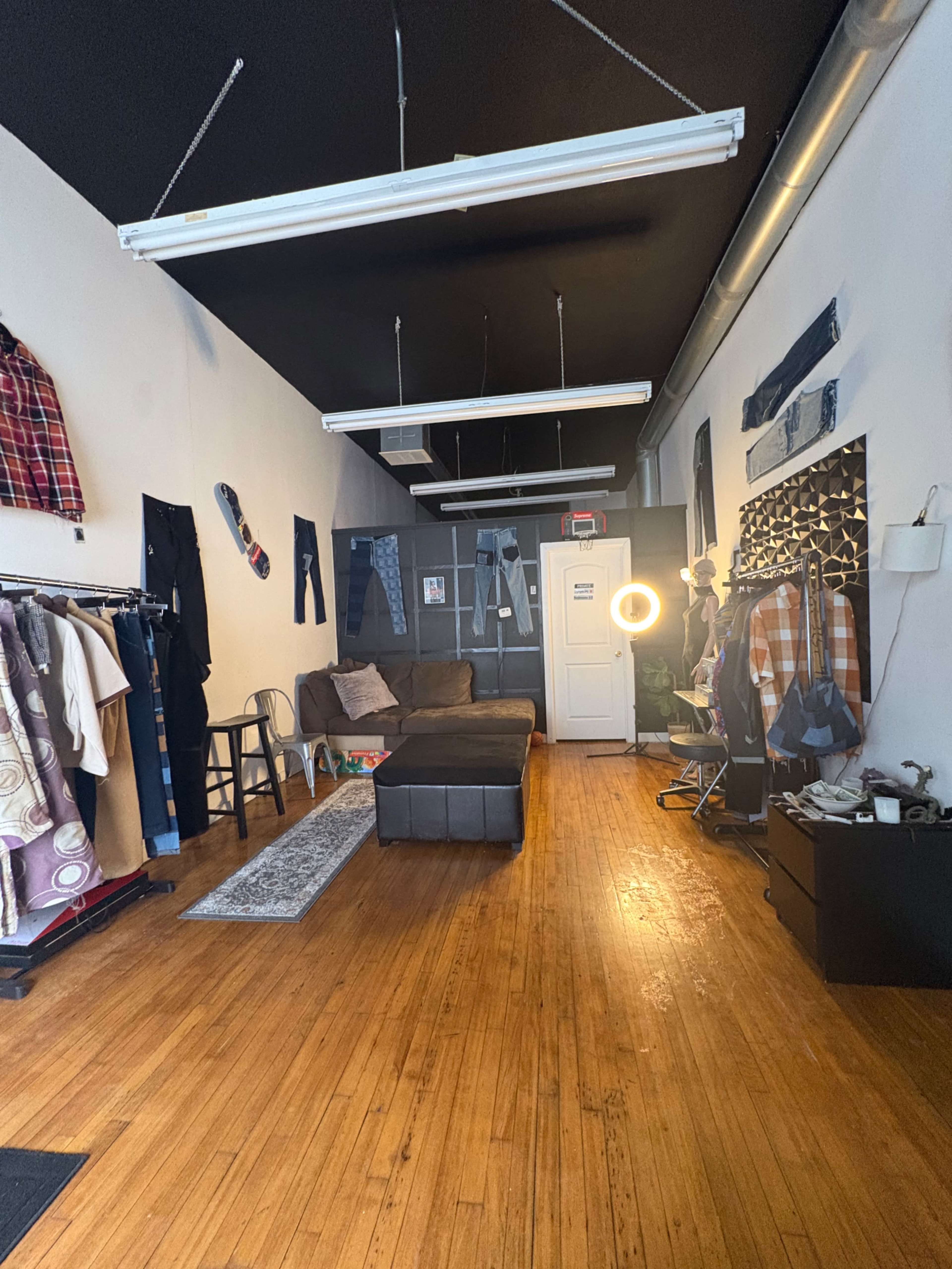 The image shows a clothing boutique featuring a couch, clothing racks, and various garments displayed on the walls in a long, narrow space with wooden floors.