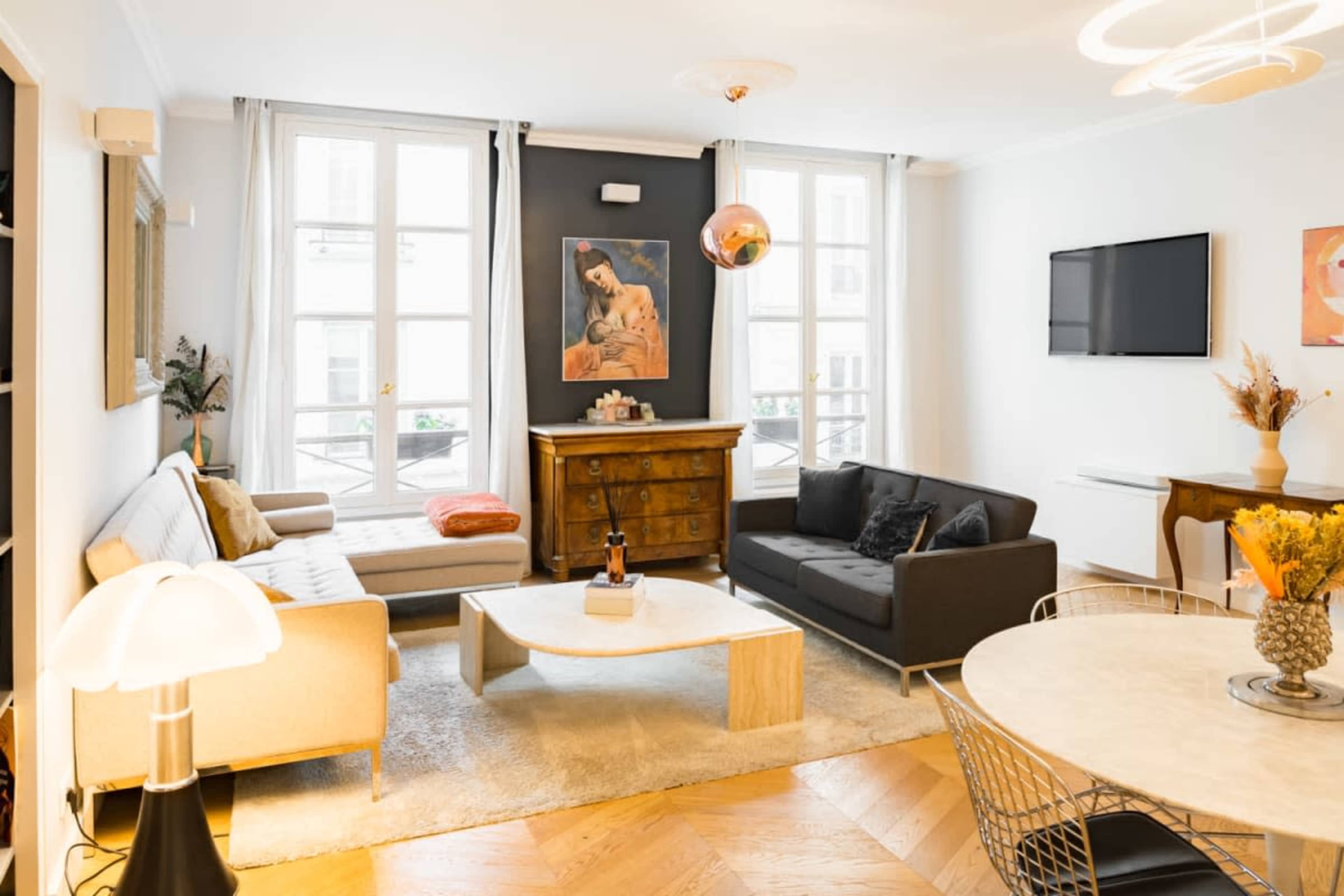 The living room features two sofas, a coffee table, a dining area with round table, and large windows letting in natural light.