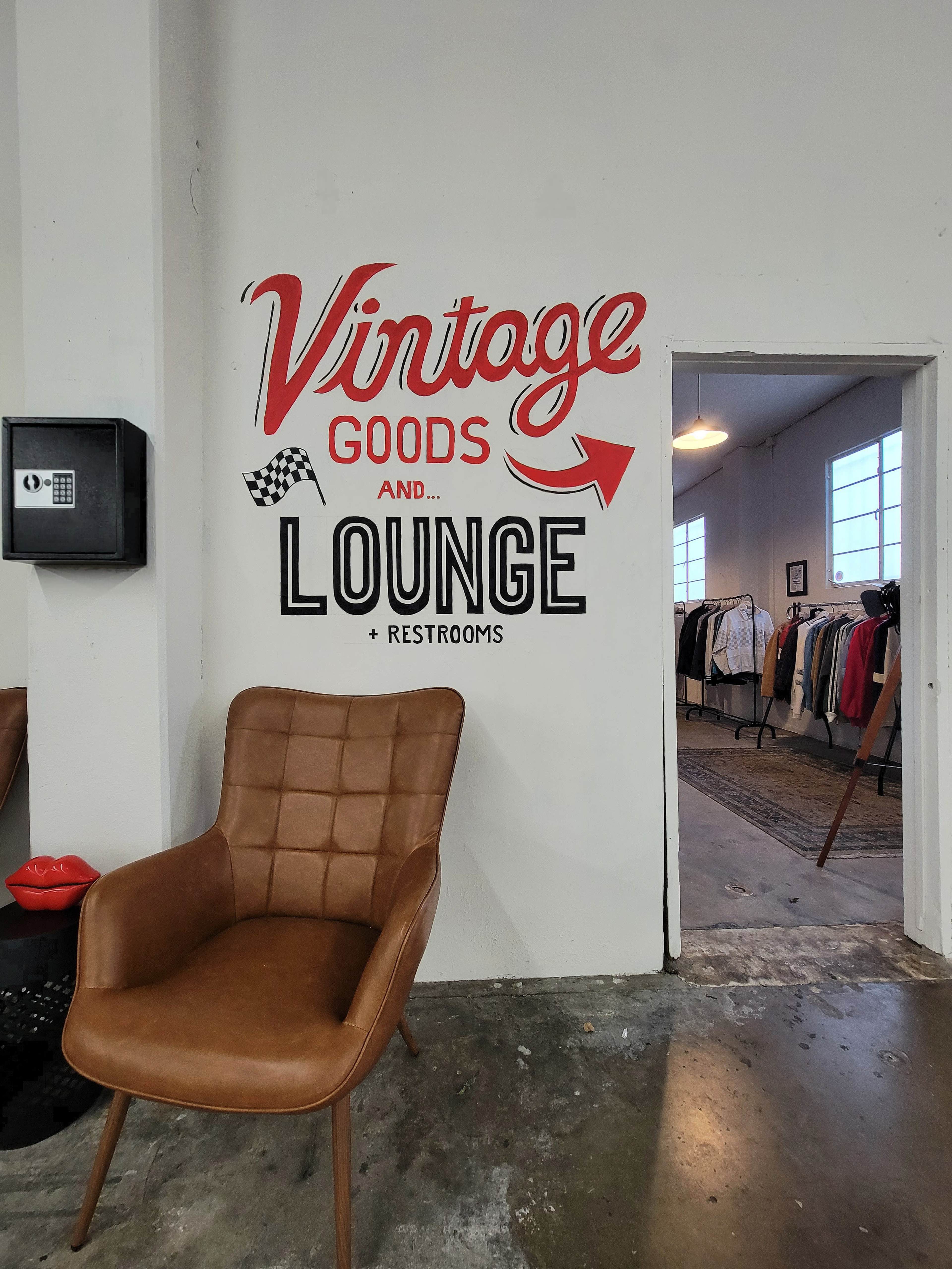 The image shows a wall with the text "Vintage Goods and Lounge" decorated with a graphic arrow, adjacent to an open door leading to a clothing area.