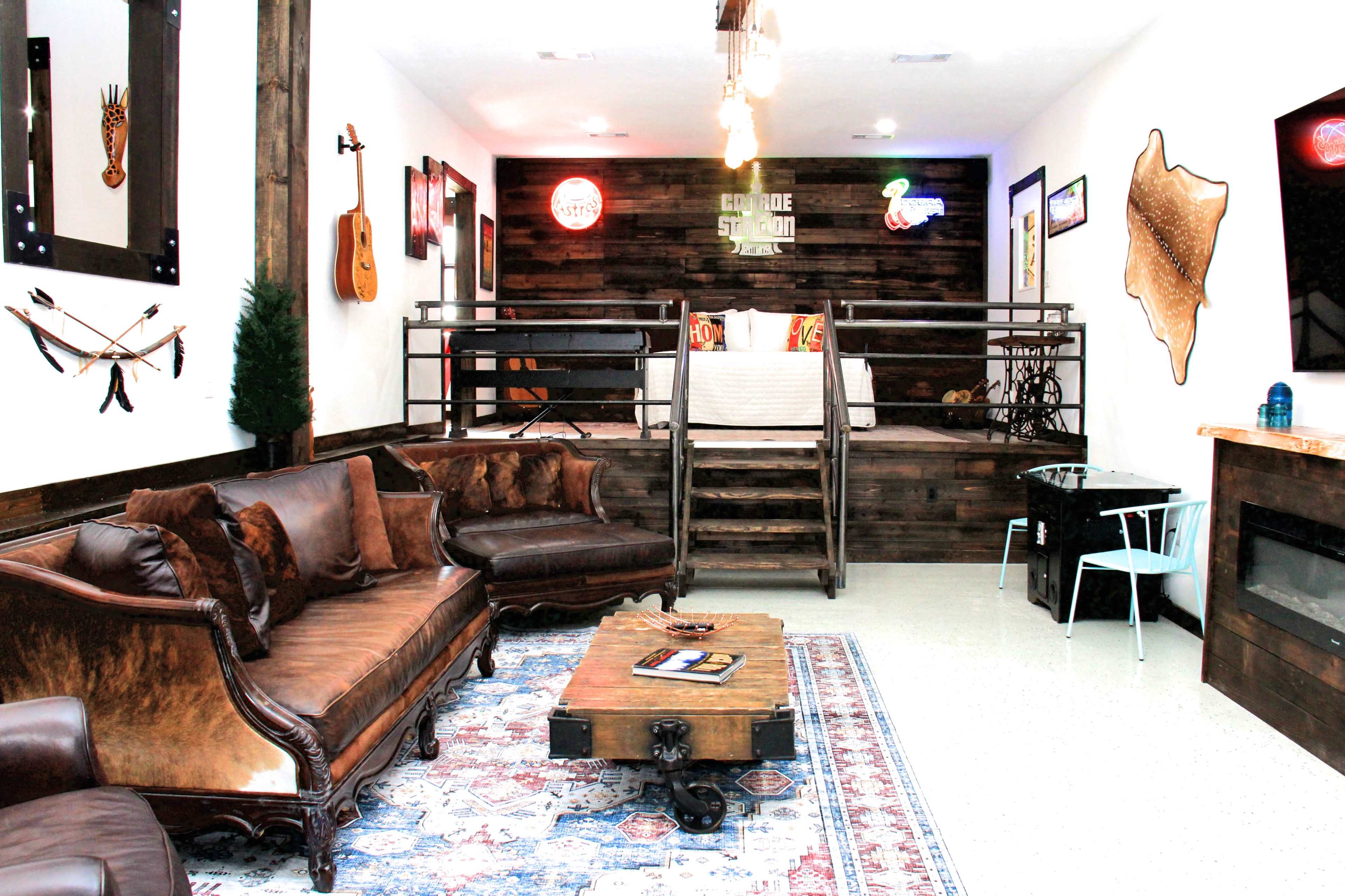 A rustic-themed bedroom with a raised bed area, wooden walls, various decorations, and a seating area featuring a dark couch and a coffee table.
