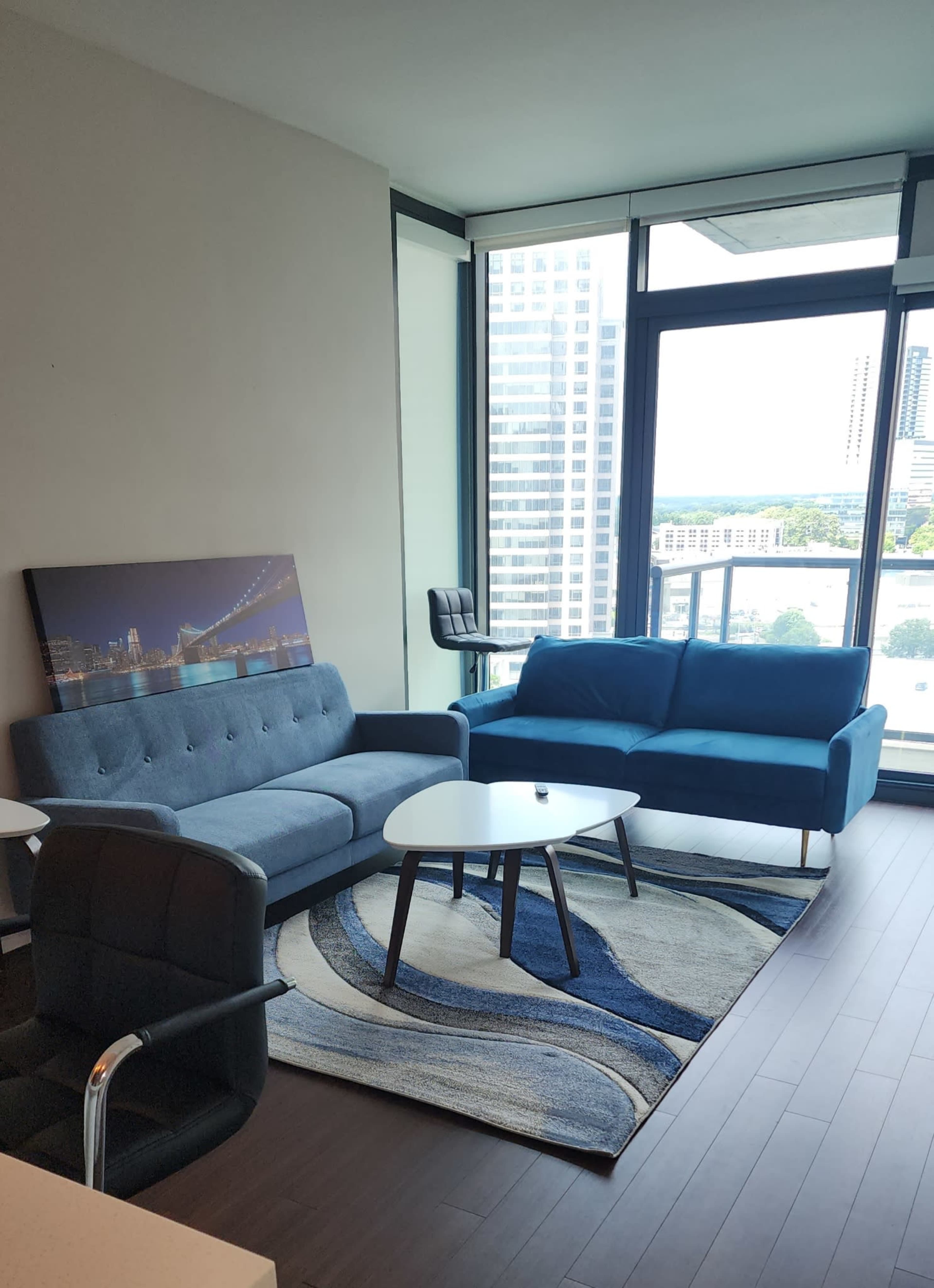 A modern living room with a blue sofa, a gray couch, a circular coffee table, and a large window overlooking a cityscape.