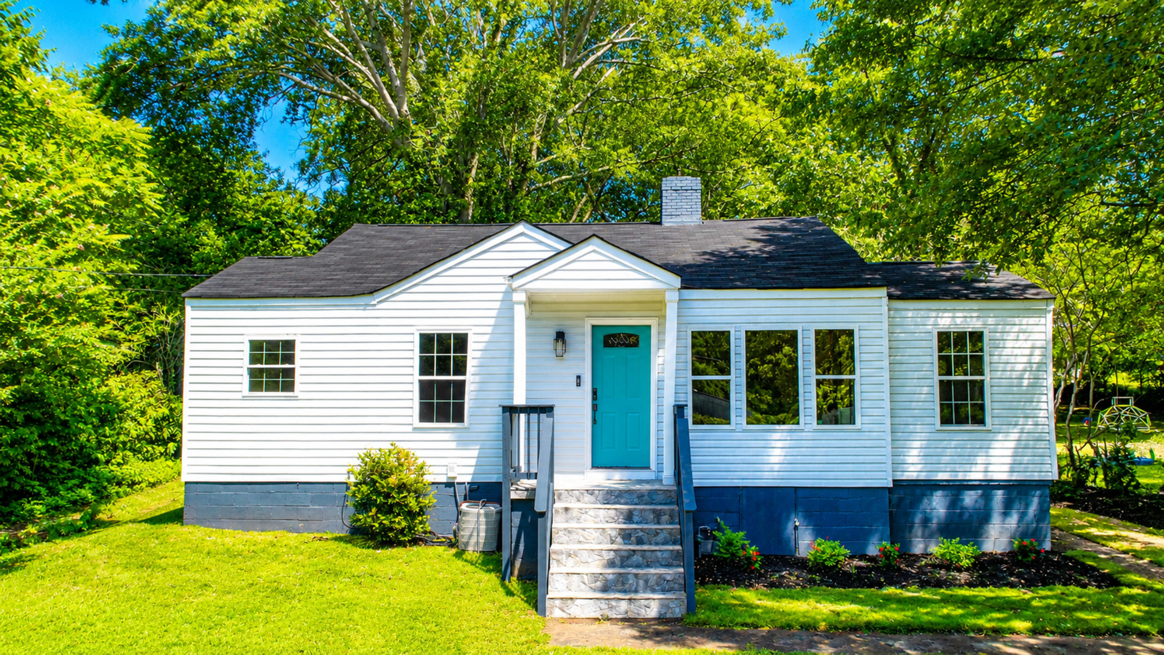 The image shows a white single-story house with a blue front door, surrounded by greenery and a well-maintained lawn.