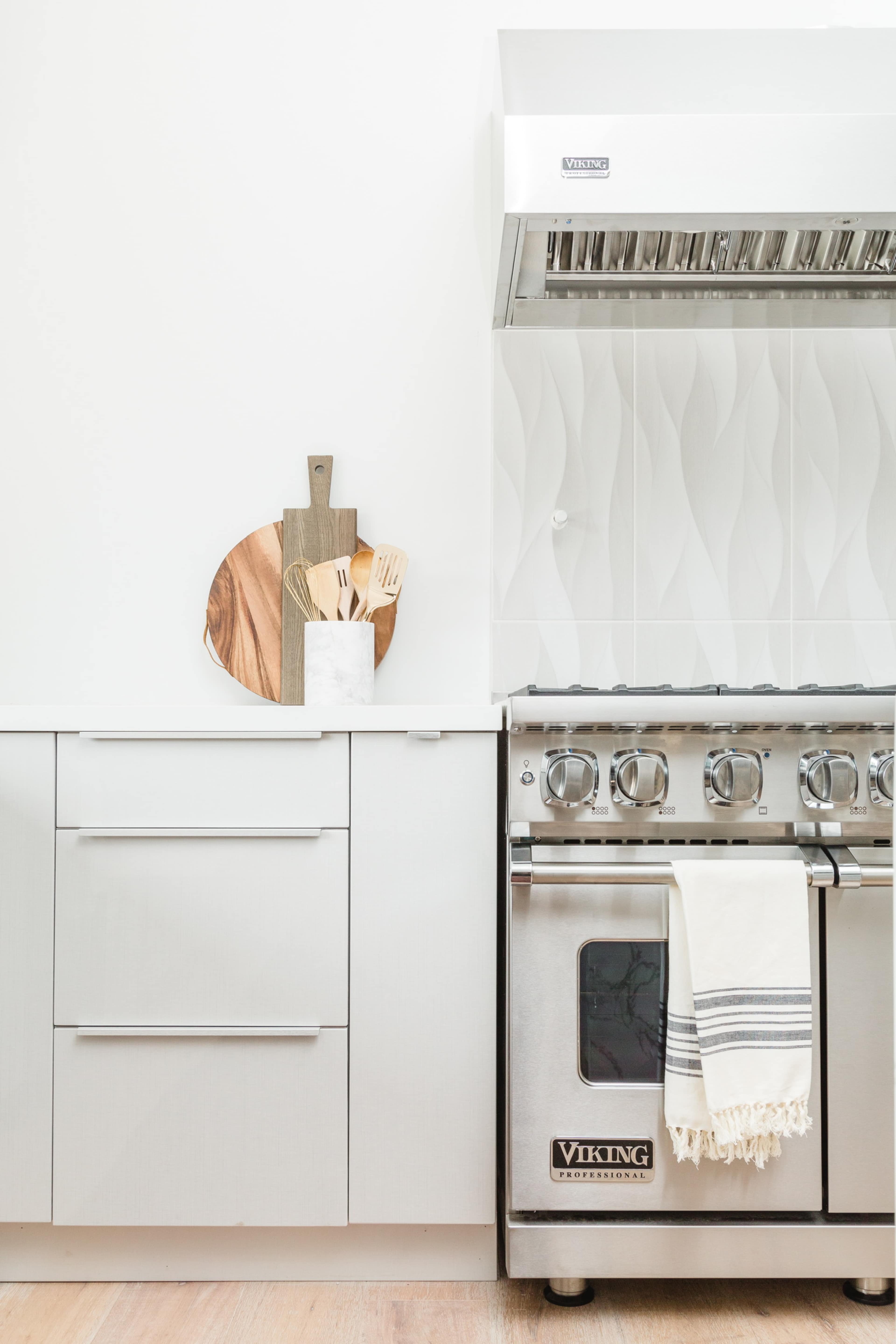 The image features a modern kitchen with a stainless steel Viking stove, sleek cabinetry, and a wooden cutting board displayed alongside cooking utensils.