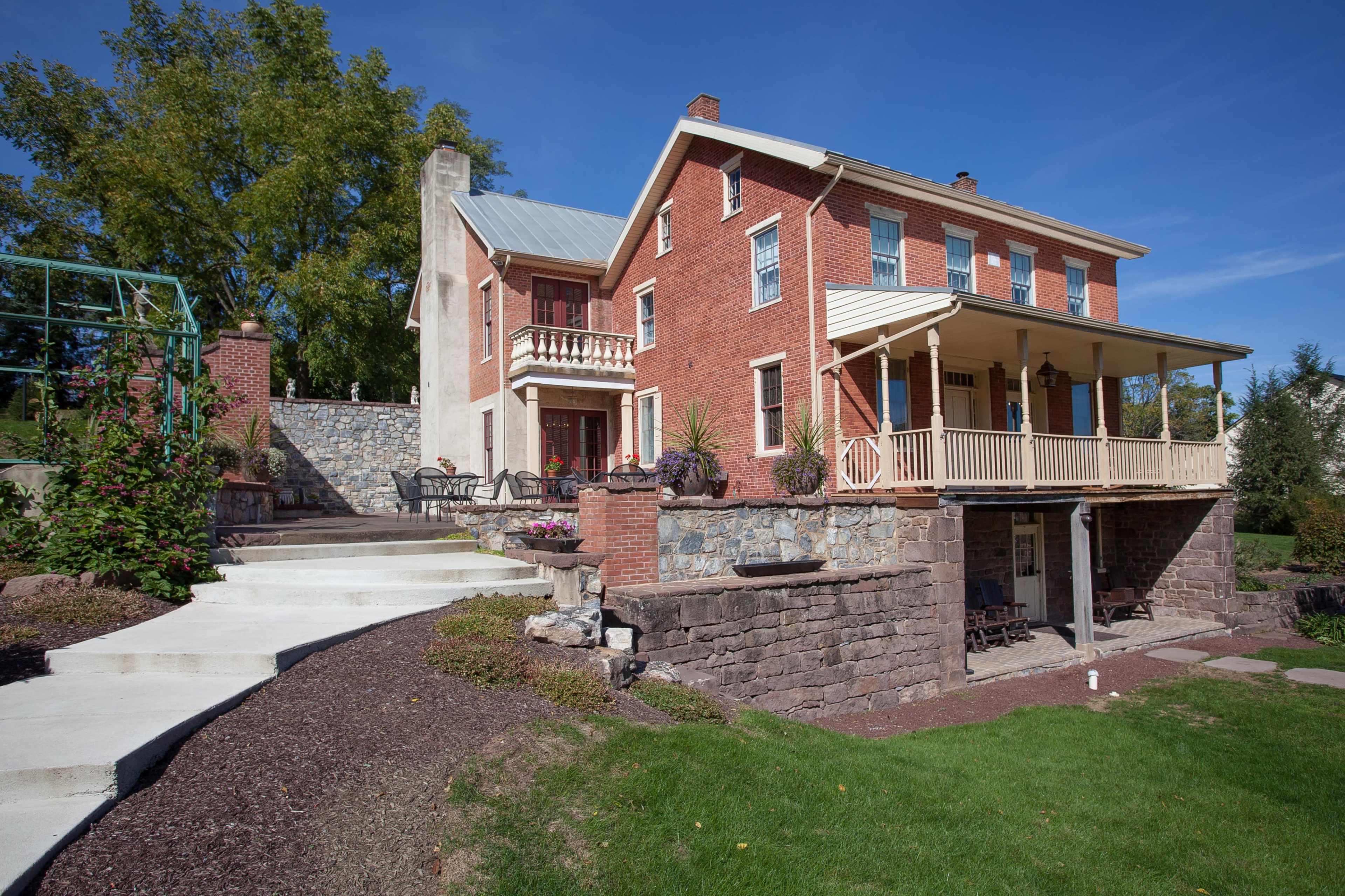 A two-story brick house with a porch, surrounded by landscaped gardens and stone pathways.