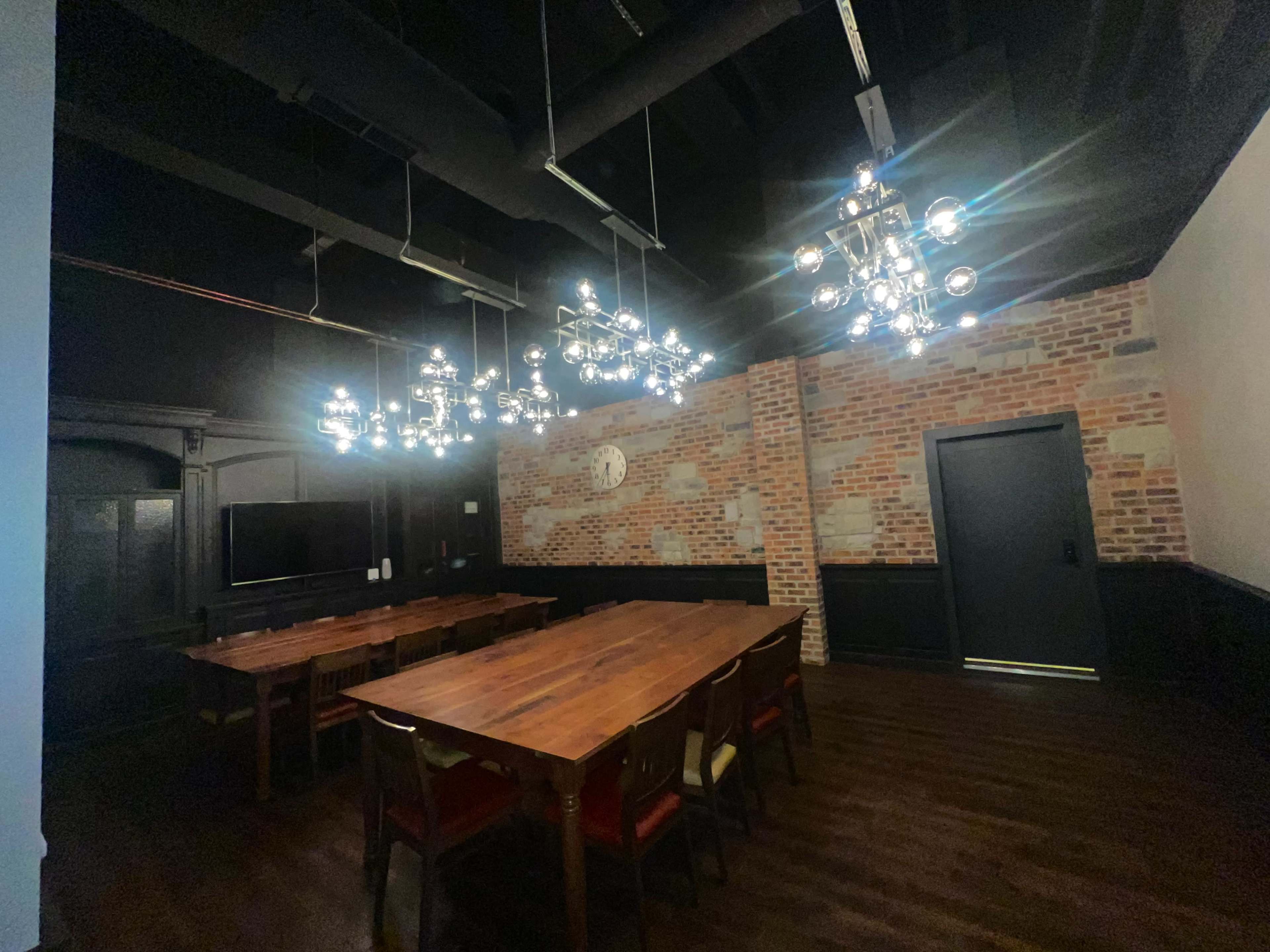 The image shows a modern conference room with a long wooden table, colorful chairs, and industrial-style chandeliers, set against a brick wall.