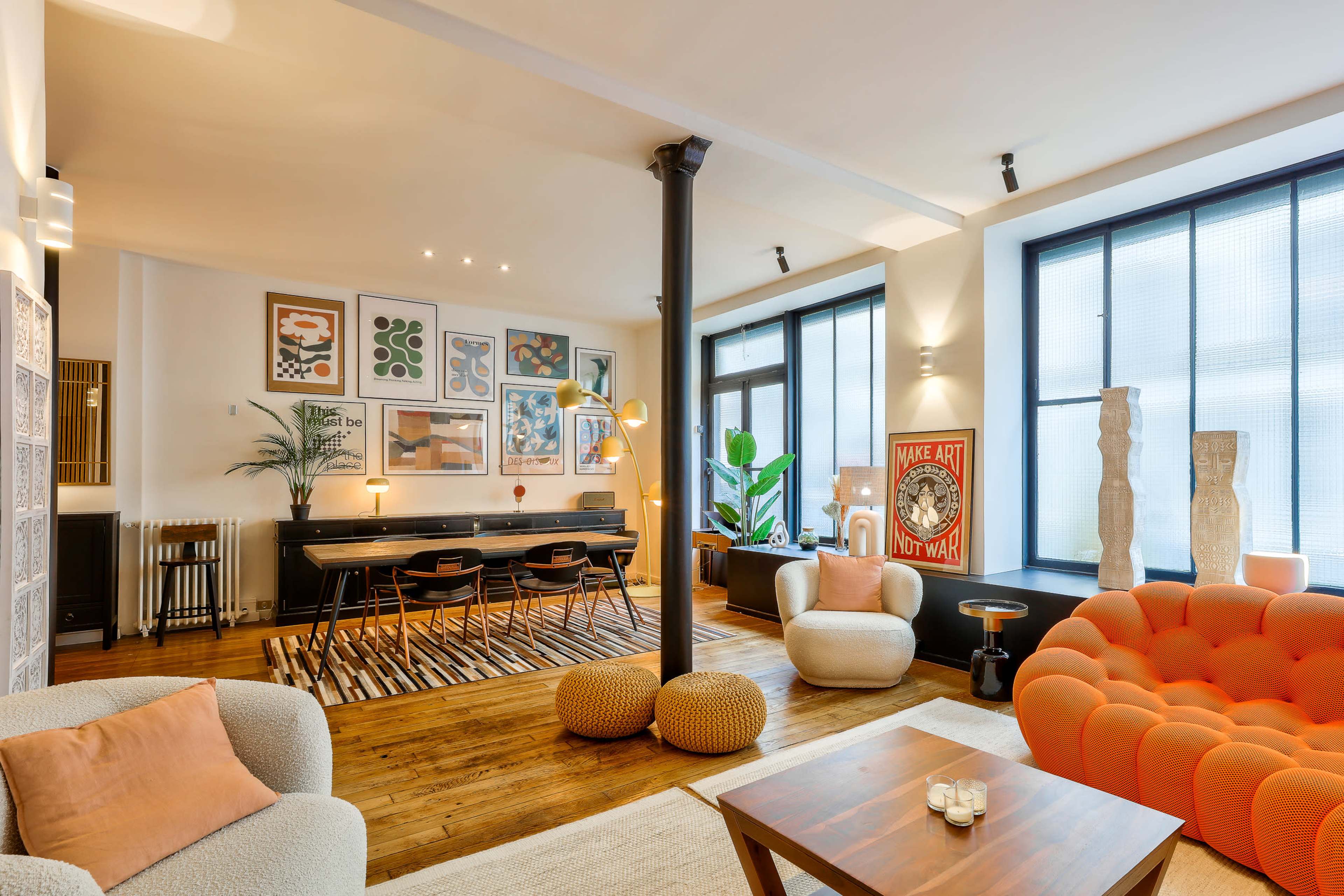 The image showcases a modern living space with a mix of seating arrangements, large windows, and vibrant artwork on the walls.