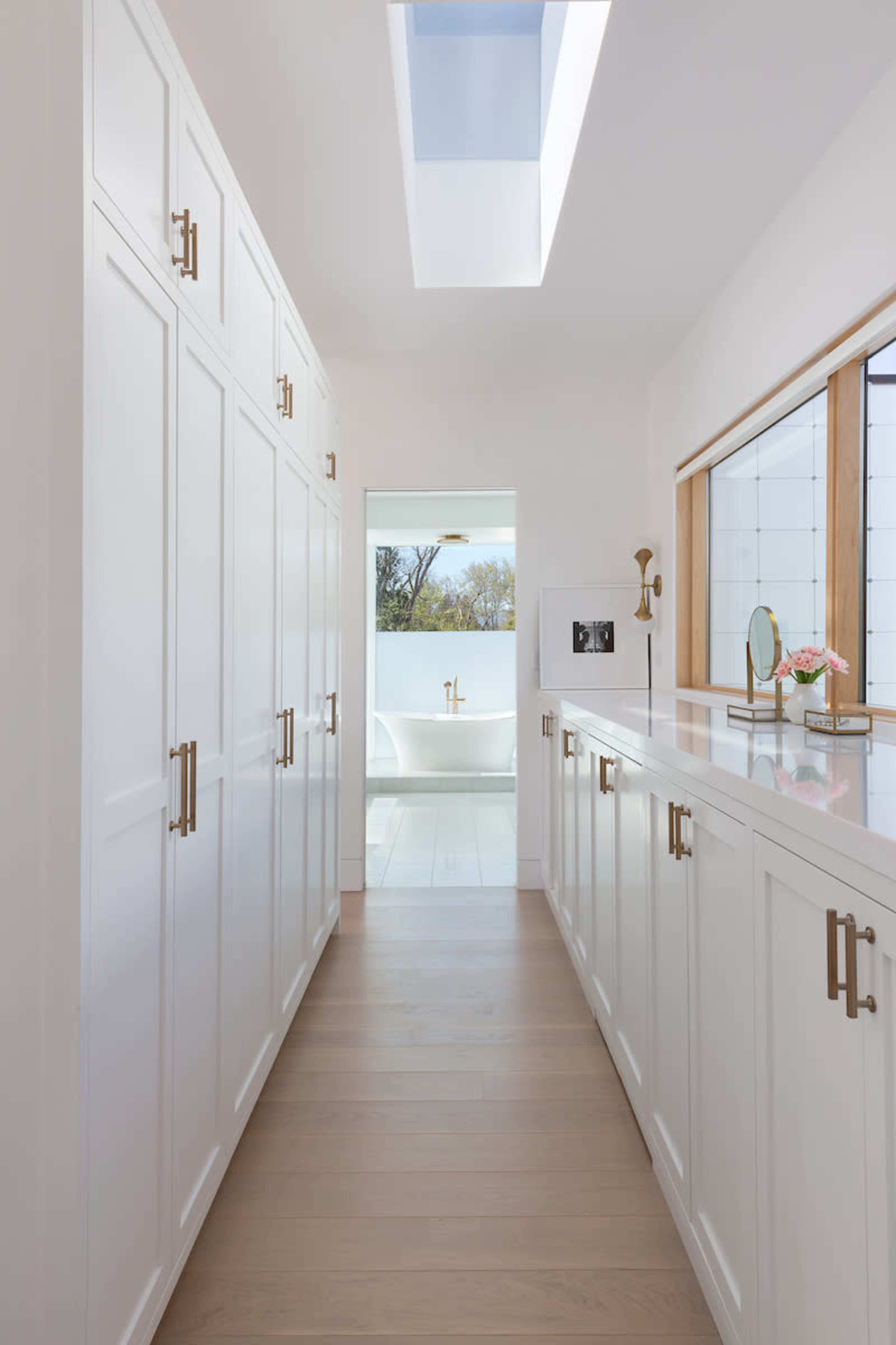 A bright hallway leading to a bathroom, featuring white cabinetry and a skylight that illuminates the space.