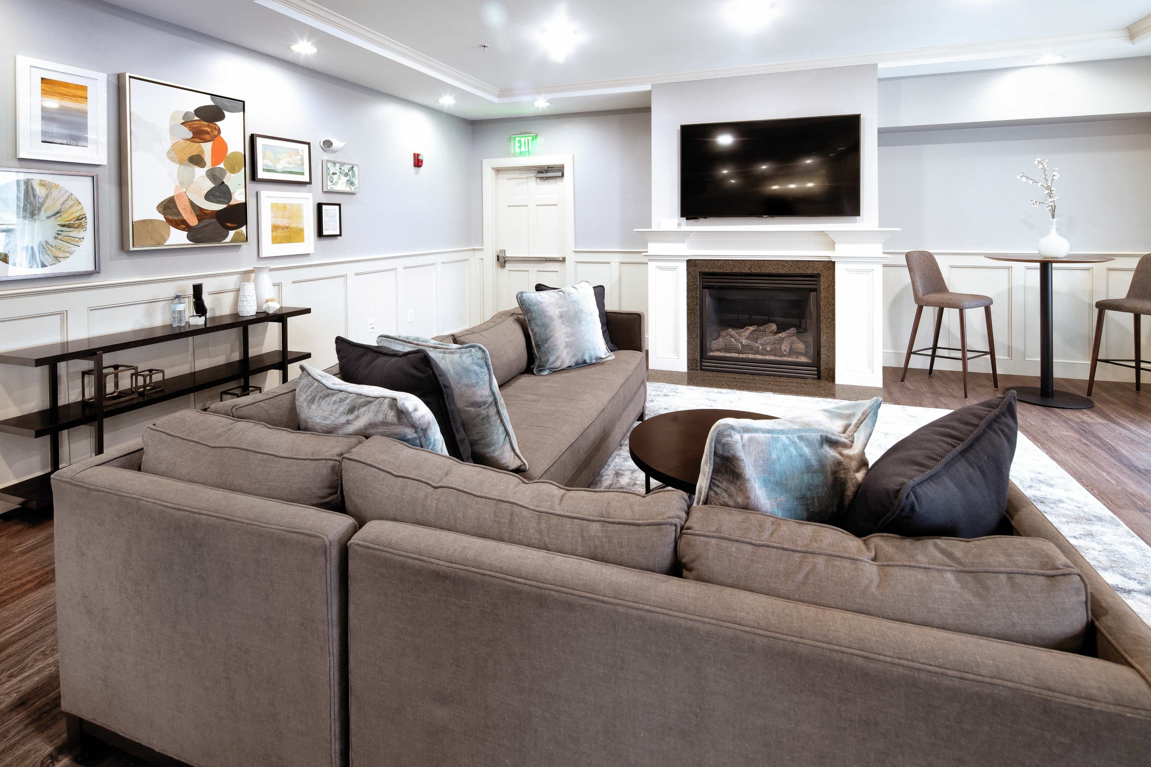 A modern living room with a sectional sofa, a coffee table, a fireplace, and a wall-mounted television, surrounded by various pieces of wall art.