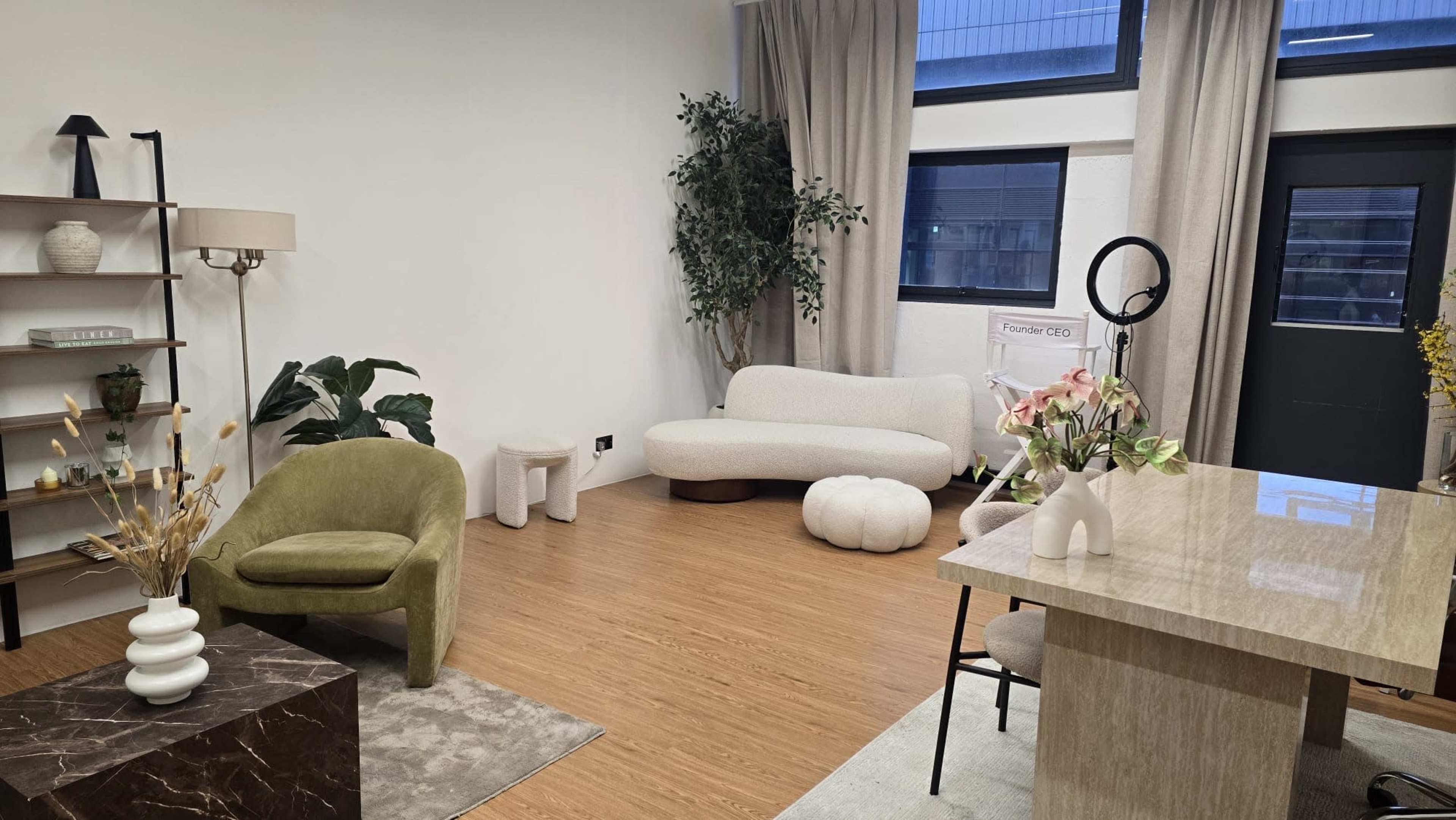The image shows a modern interior space featuring a green armchair, a white curved sofa, a small circular table, and a desk with floral arrangements.