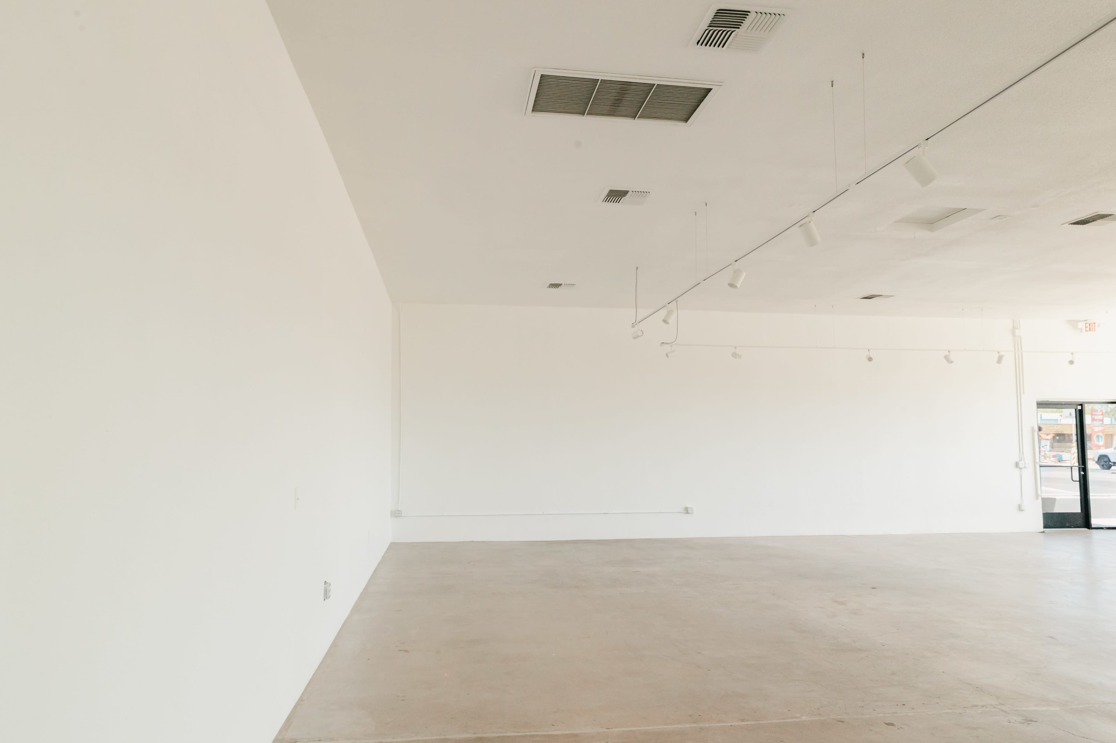 The image shows an empty room with white walls, a concrete floor, and track lighting along the ceiling.