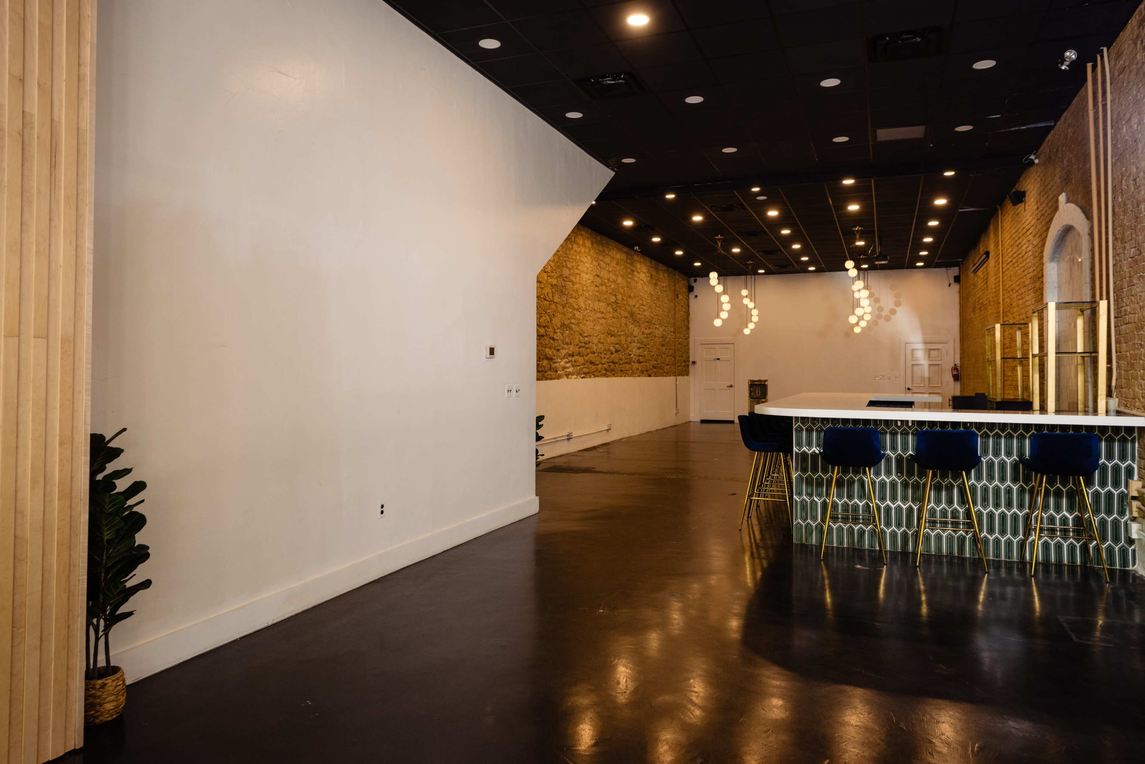 The image shows a spacious interior with a bar area featuring patterned tiles, minimalist furnishings, and exposed brick walls.