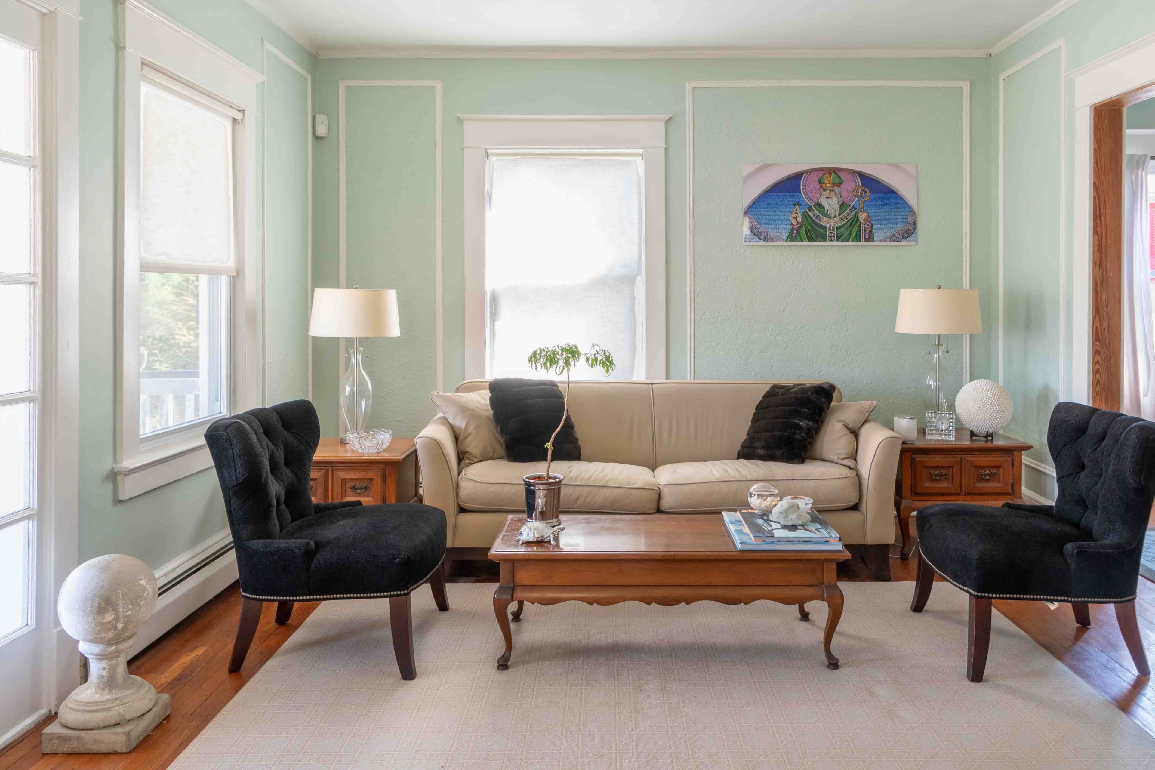 A light green living room features a beige sofa, two black armchairs, a coffee table, and lamps on wooden side tables.