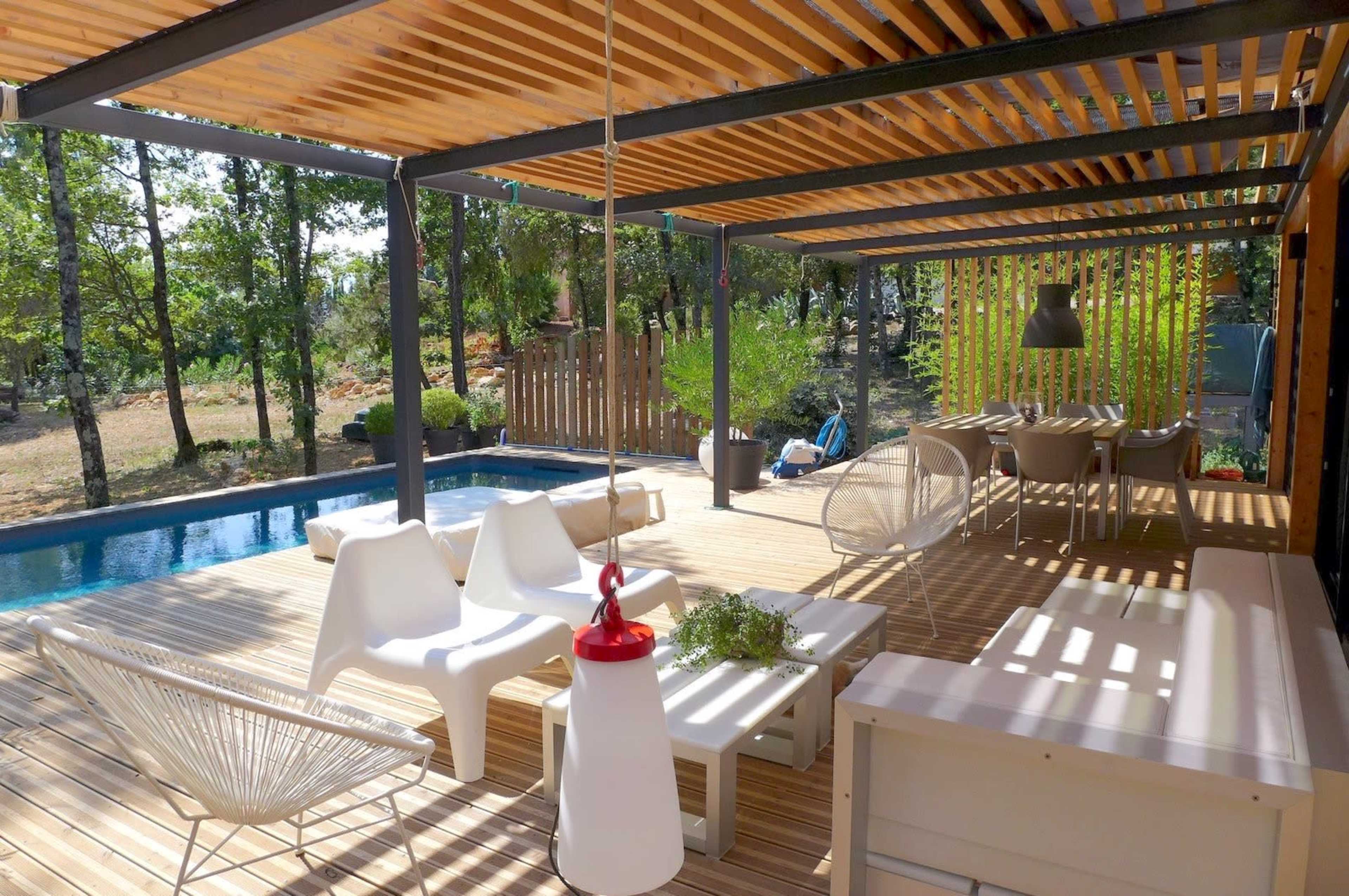 A wooden deck with modern furniture surrounds a swimming pool, featuring shaded seating areas and decorative plants.